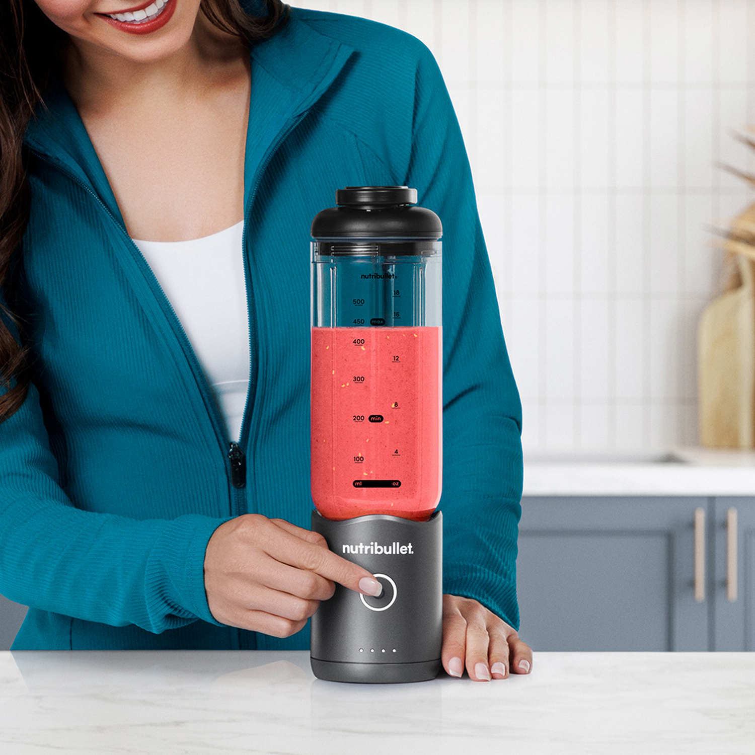 Una mujer presiona un botón en una licuadora Nutribullet gris con un batido rojo.