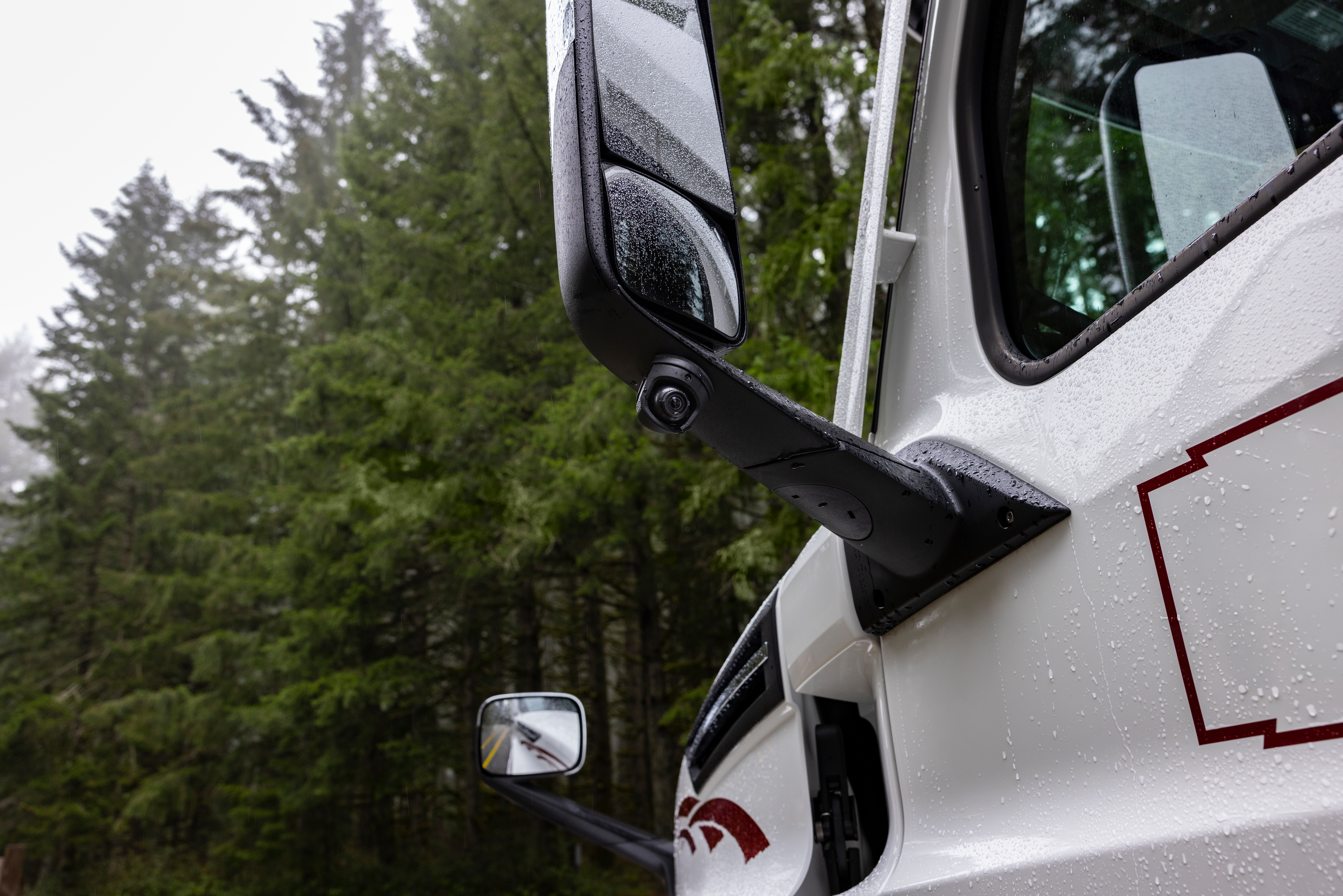 Specchietto bianco per camion con gocce di pioggia, foresta verde sullo sfondo.