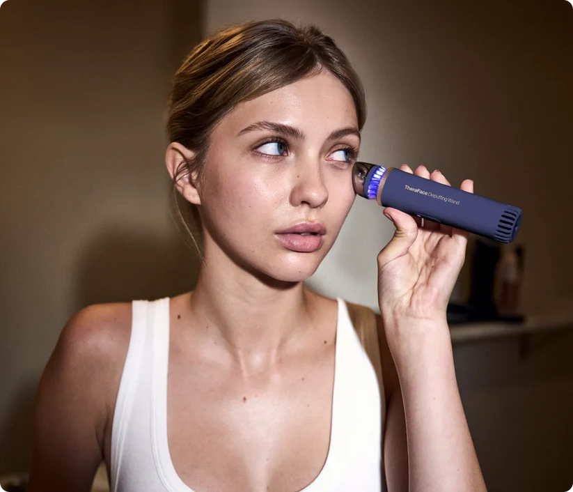 Una mujer usa un dispositivo azul TheraFace cerca de su ojo.