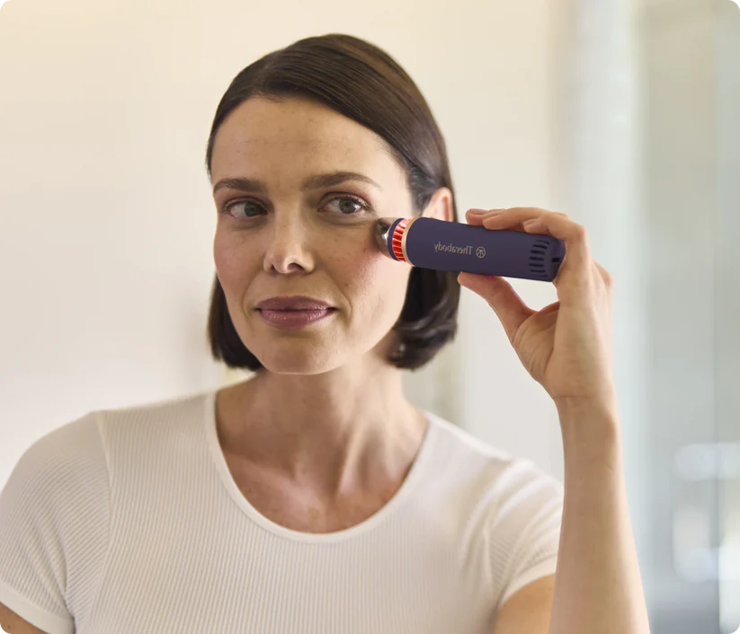 Una mujer usa un dispositivo de cuidado de la piel azul cerca de su ojo.