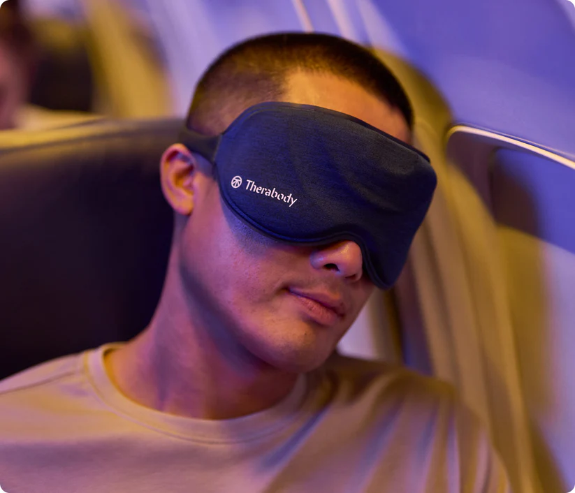 Hombre con antifaz oscuro sentado en un avión, durmiendo.