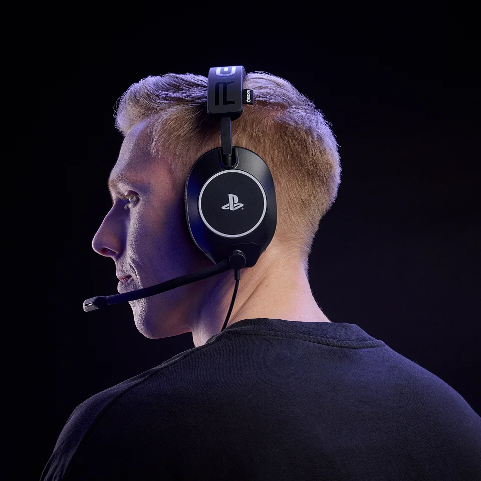 Ein Mann mit blonden Haaren trägt schwarze Kopfhörer mit Mikrofon. PS-Logo.