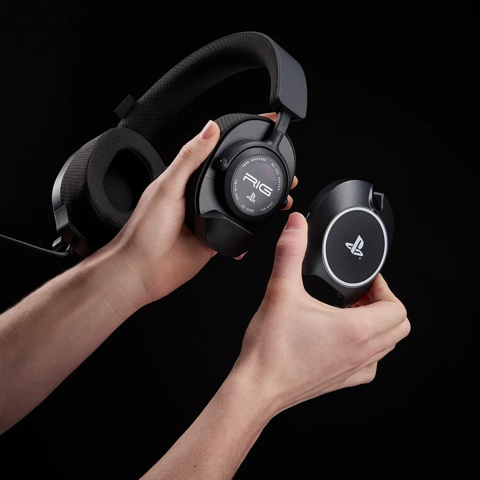 Hände halten schwarze Gaming-Kopfhörer und ein rundes PlayStation-Headset-Teil.