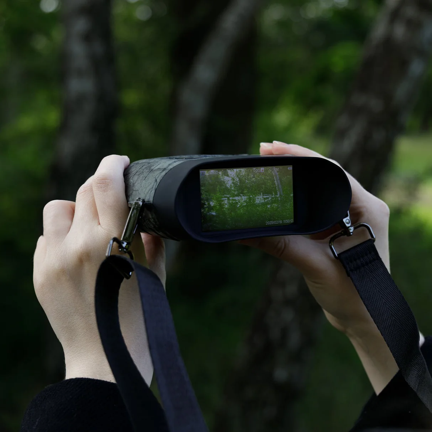 Person holds binoculars with a screen showing a green landscape.