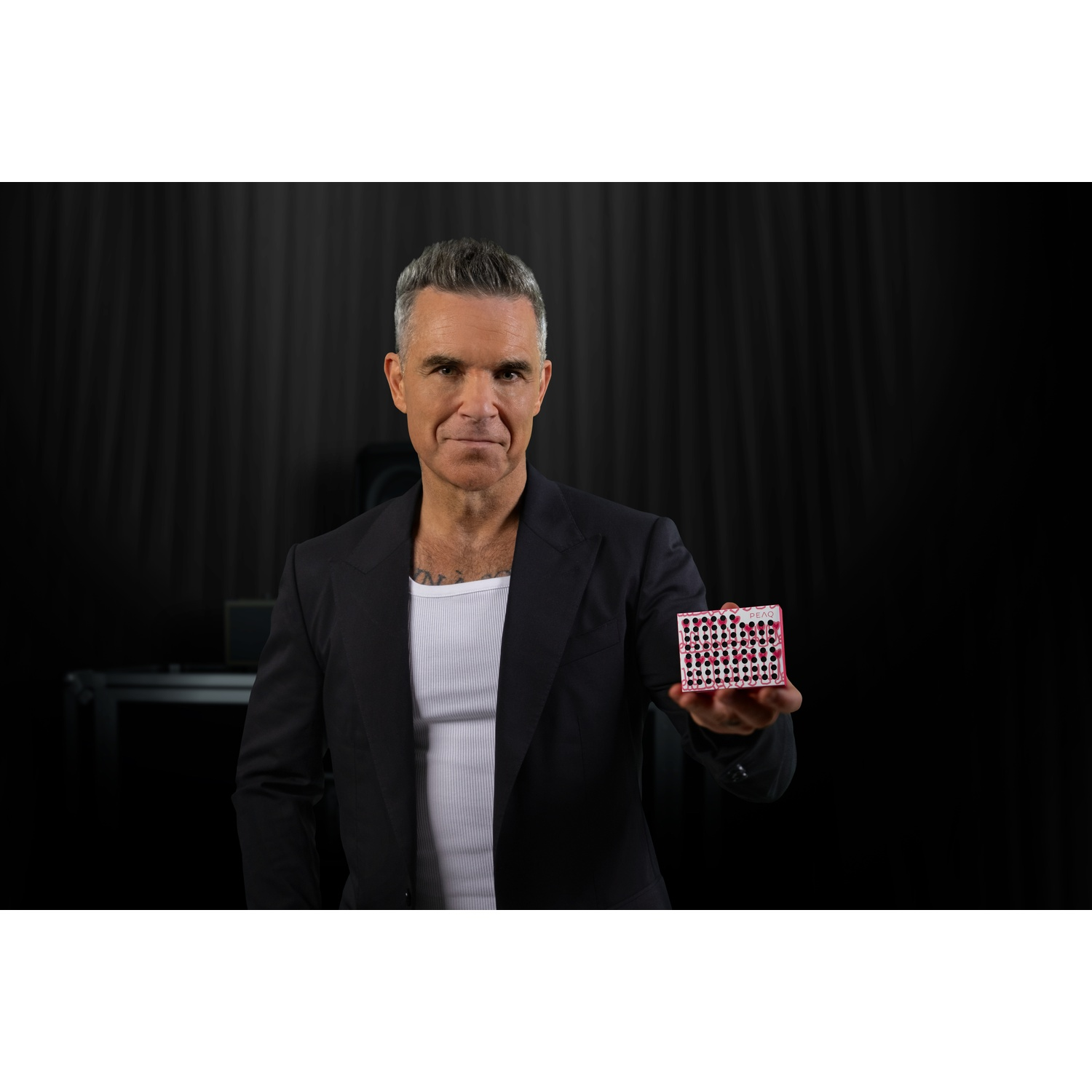 Man in a black suit holds a small white box decorated with red hearts.