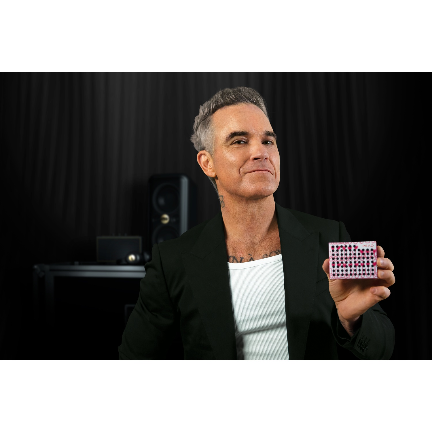 Man with gray hair in a black suit holds a card with hearts and dots.