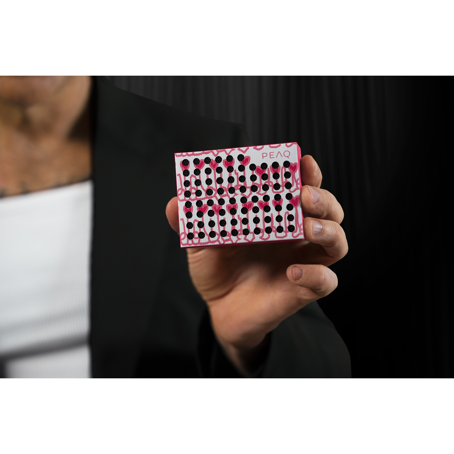 A hand holds a white box with black dots and pink hearts.