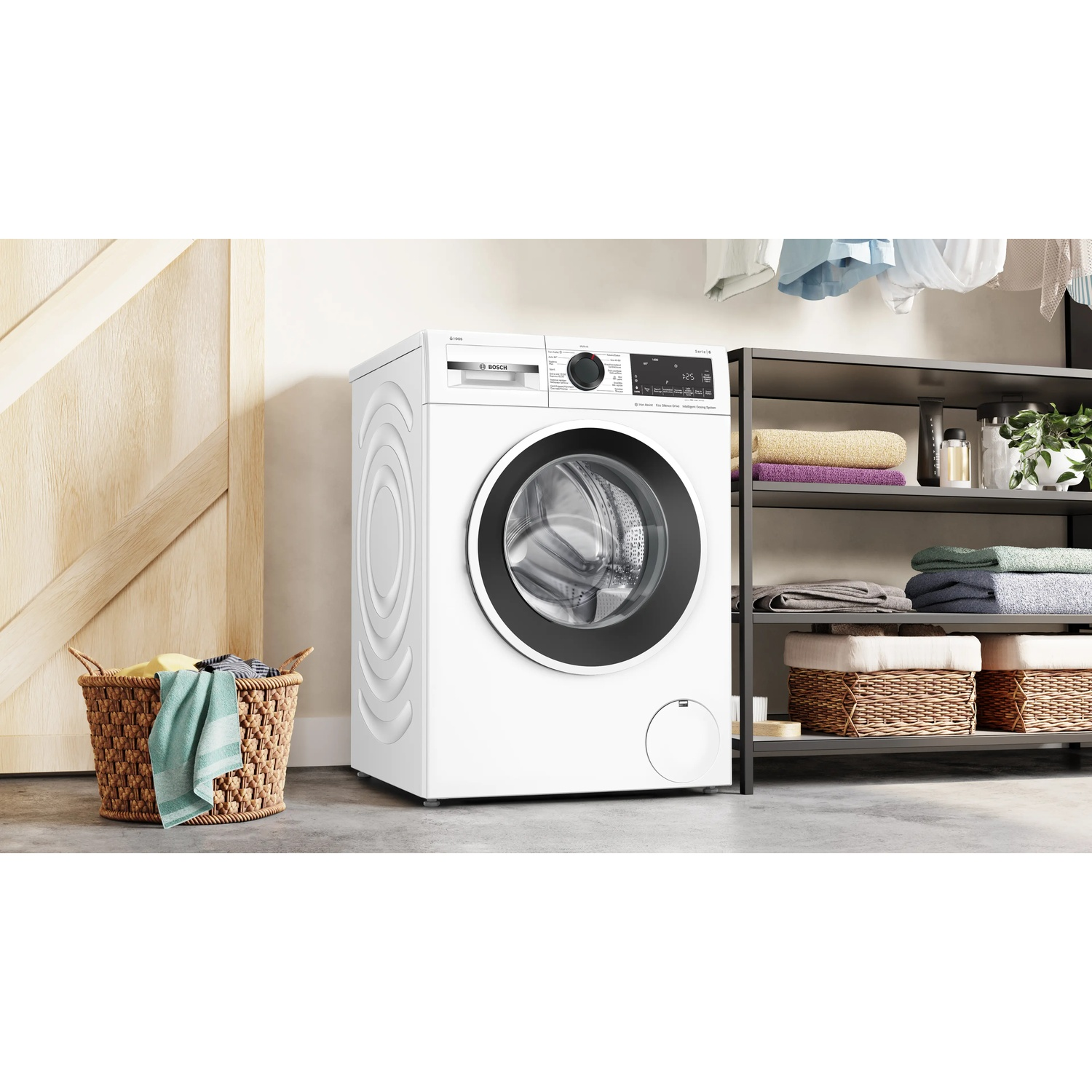 A white washing machine is next to a laundry basket and a shelf with towels.