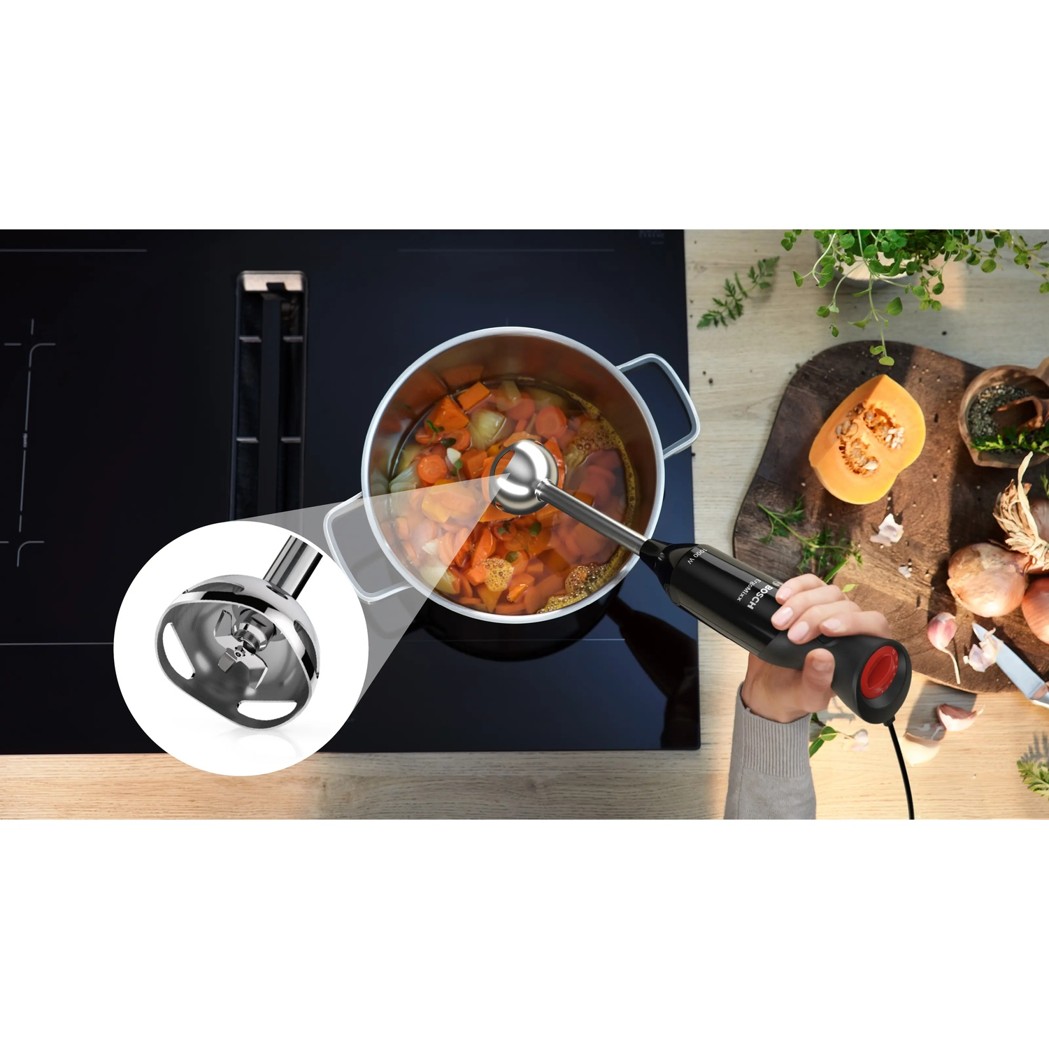 Hand blender with attachment over pot of vegetables on stovetop, next to pumpkin and onions.