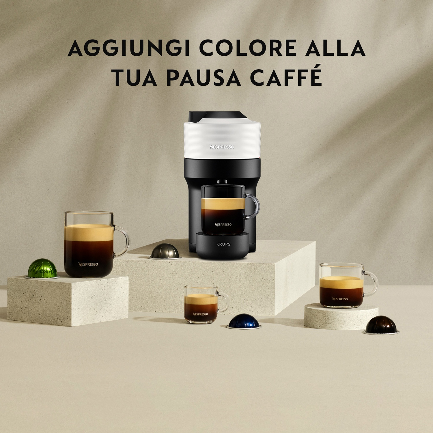 Macchina da caffè Nespresso con tazze e capsule su sfondo neutro.