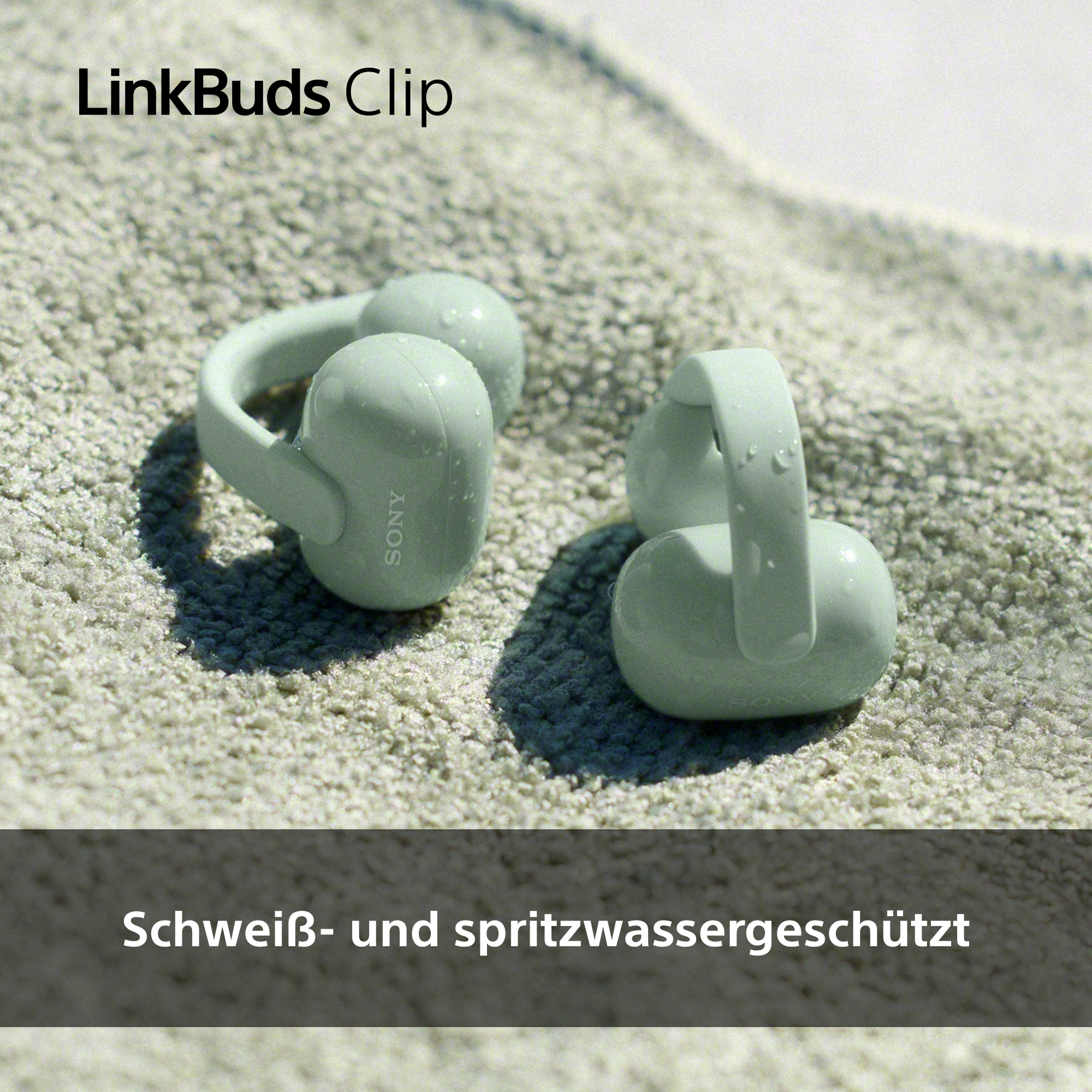 Zwei hellgrüne Sony LinkBuds Clip Ohrhörer mit Wassertropfen auf einer strukturierten Oberfläche.