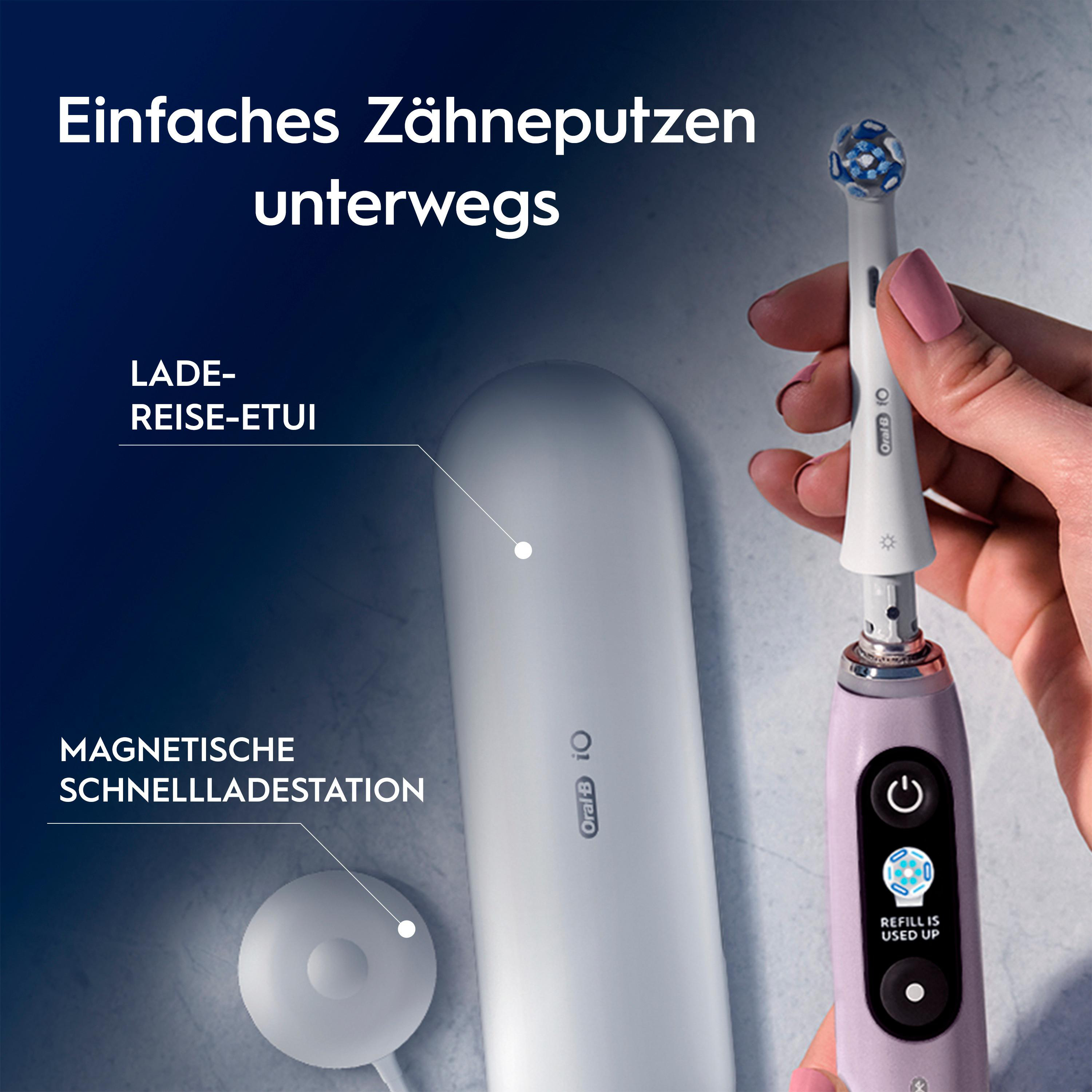 Eine Hand hält eine elektrische Zahnbürste mit Aufsatz. Reise-Etui und Ladestation daneben.
