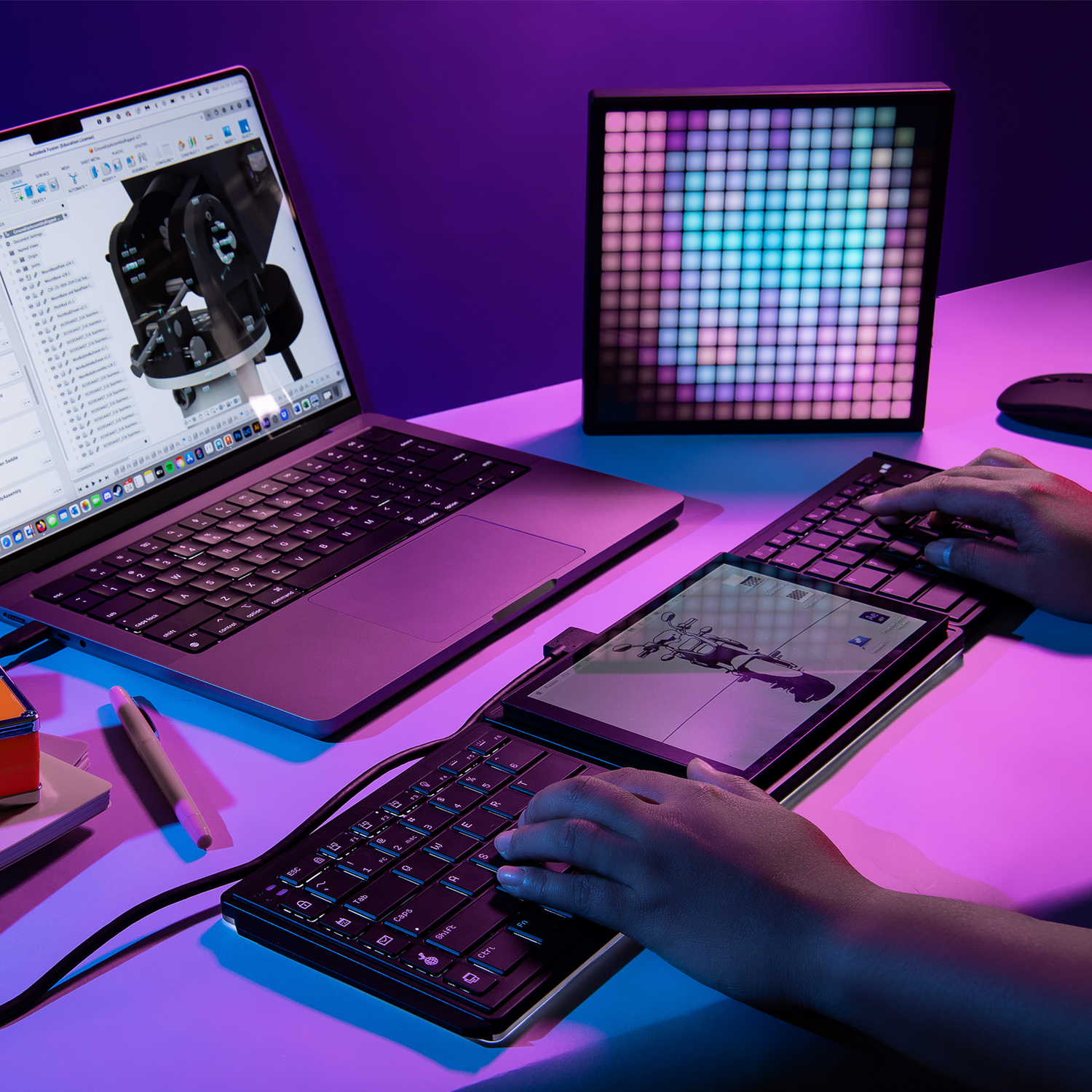 A person uses a keyboard and tablet in front of a laptop and a light-up display.