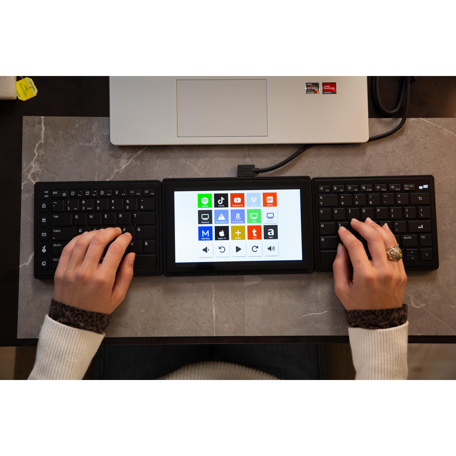 Person types on a split keyboard with a central touchscreen and laptop.