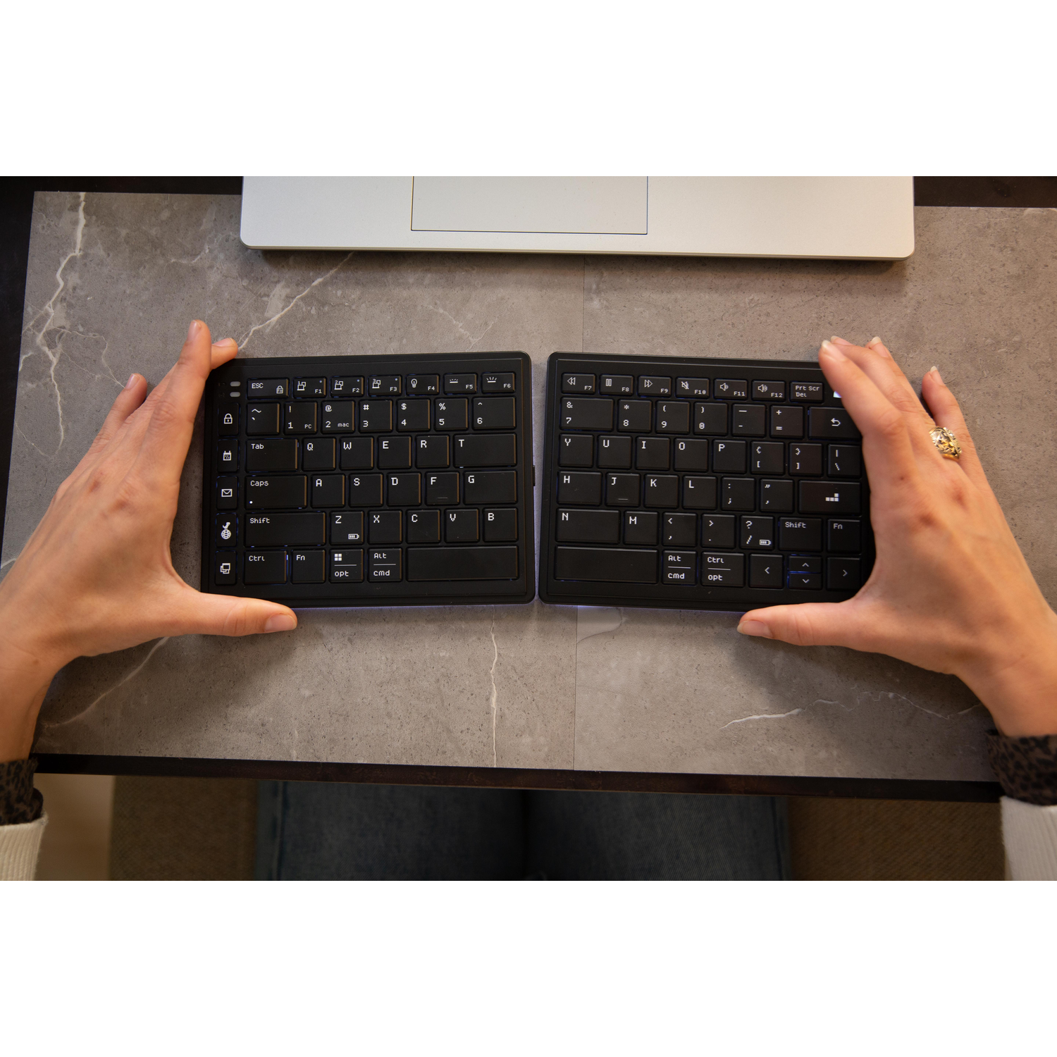 Two black keyboards on a desk, held by hands.