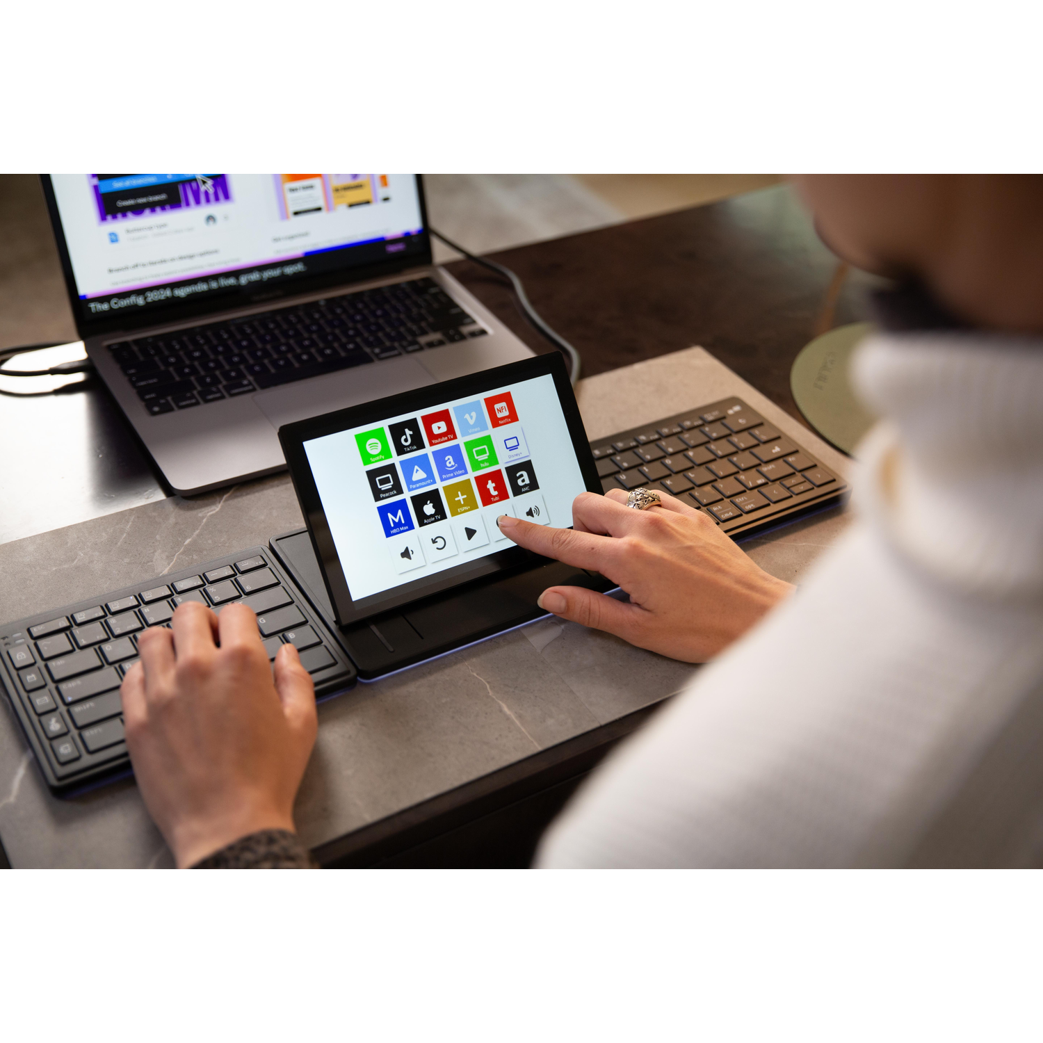 A person touches a touchscreen with app icons next to a laptop.