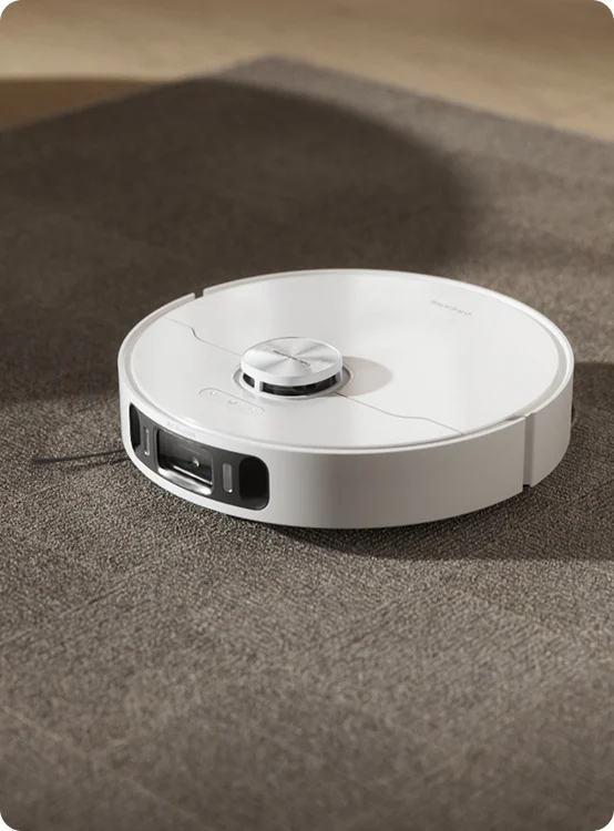 Biały robot sprzątający na szarej wykładzinie.