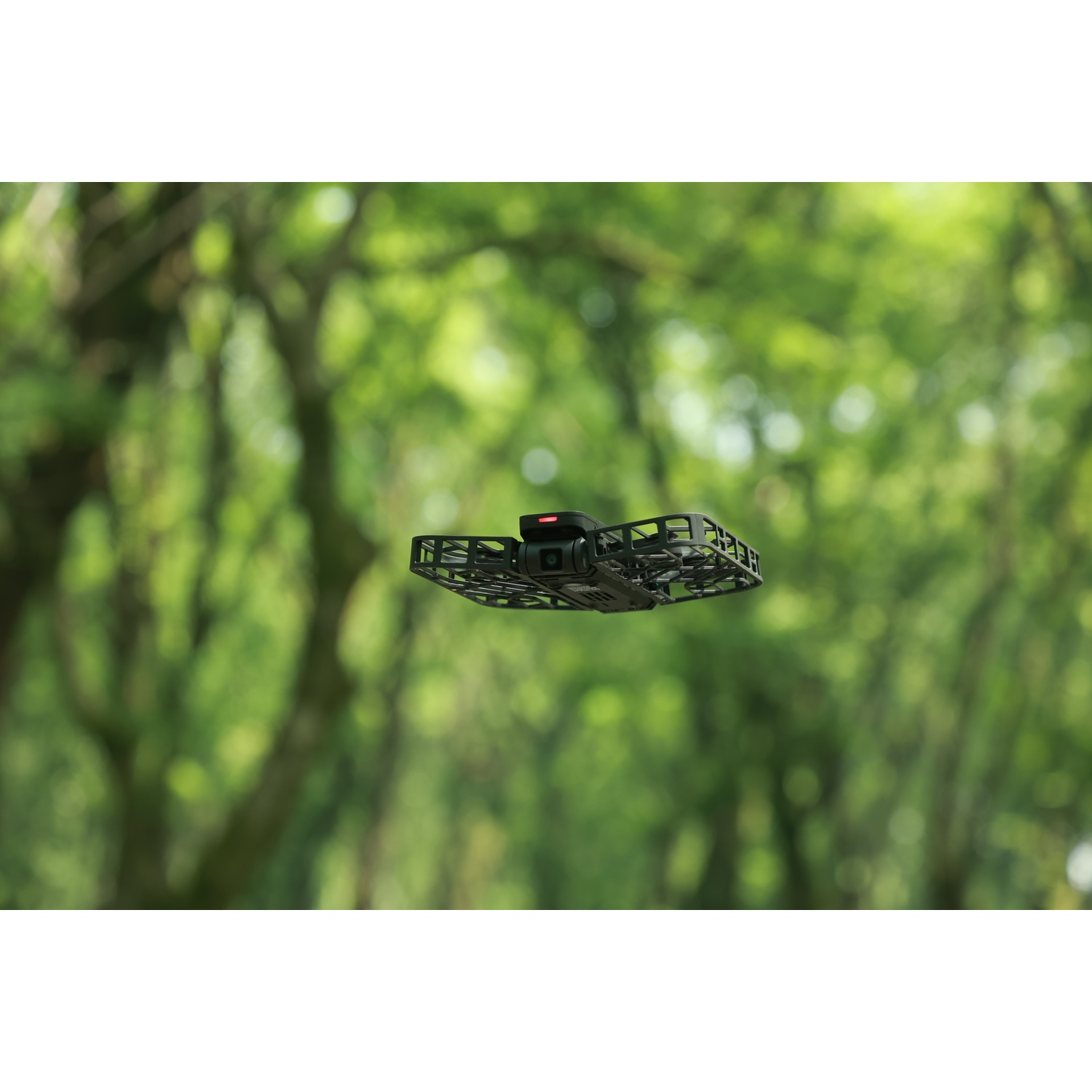 Een zwarte drone vliegt voor een wazige groene achtergrond van bomen.