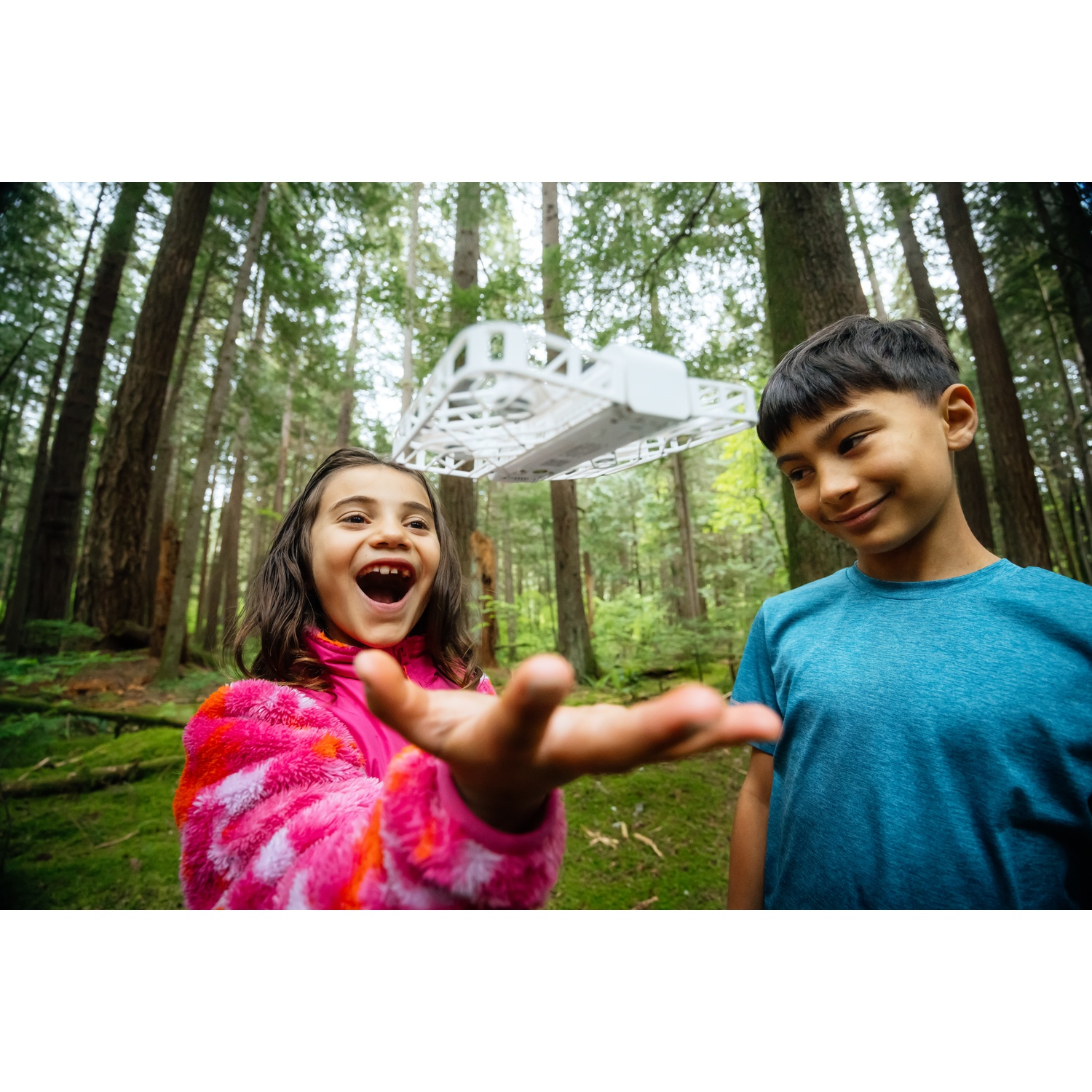 Twee kinderen in een bos met een drone die erboven zweeft.