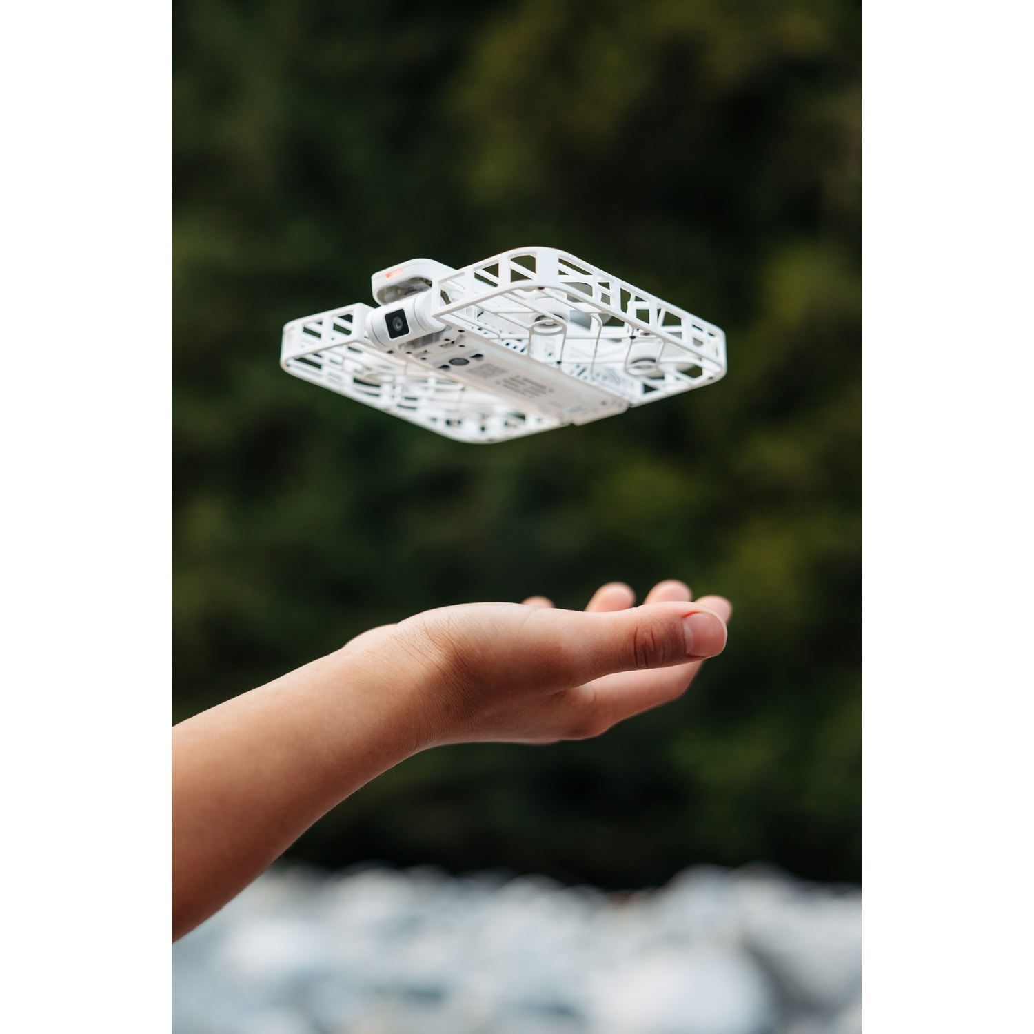 Een witte drone zweeft boven een open hand, met een wazige groene achtergrond.
