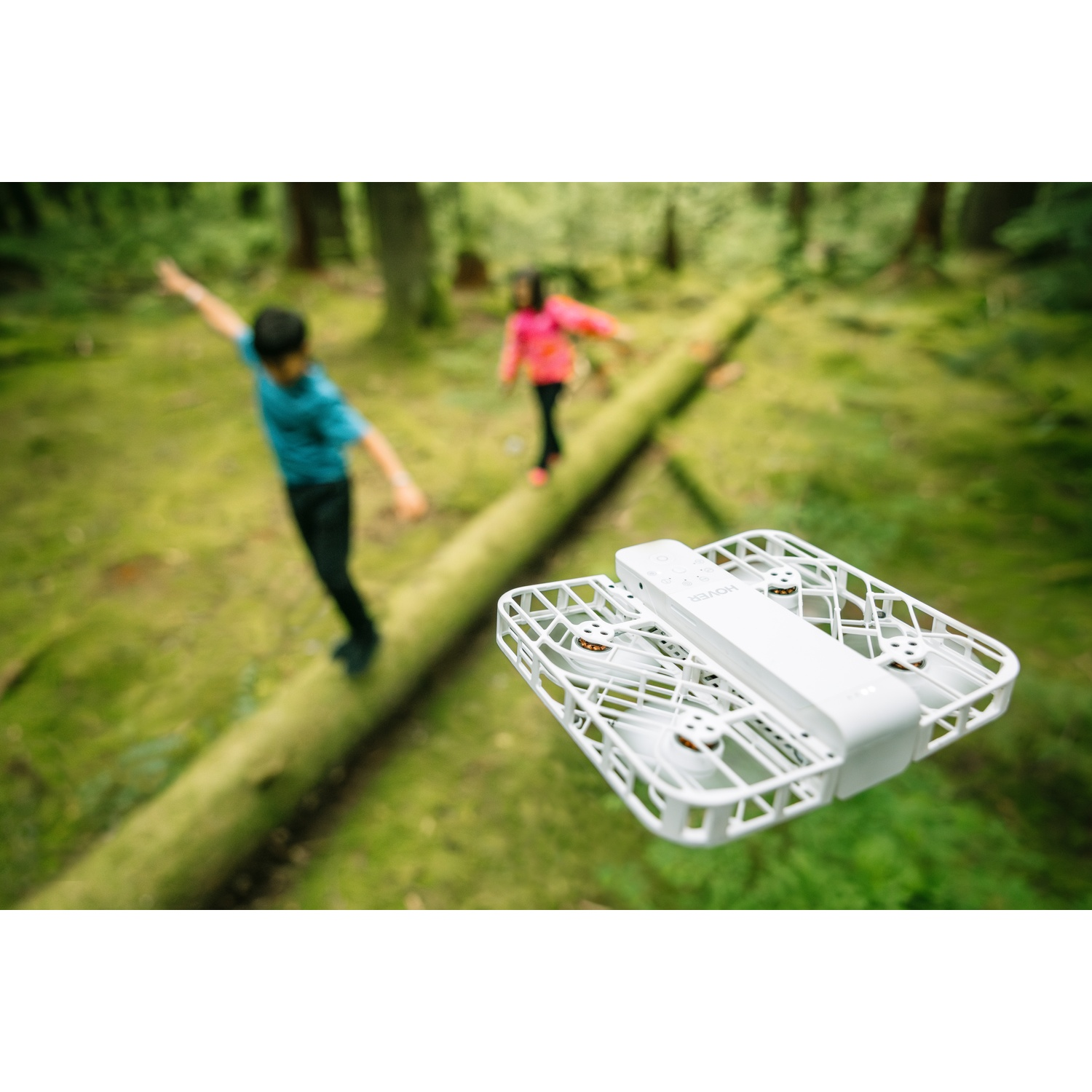 Een witte mini-drone vliegt boven een bemoste boomstam in een bos.
