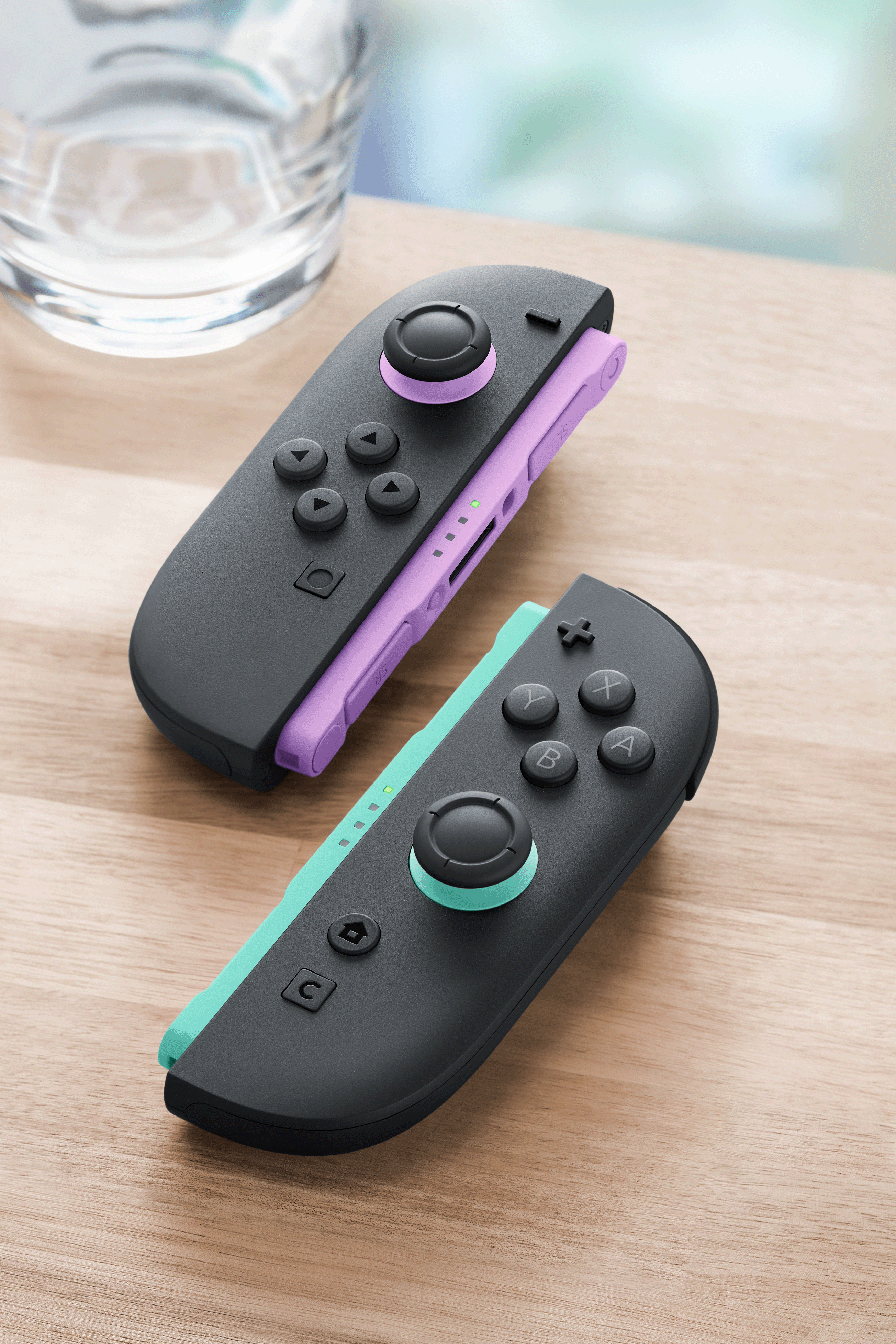 Zwei Nintendo Switch Joy-Cons liegen auf einem Holztisch, einer in Lila, der andere in Türkis.