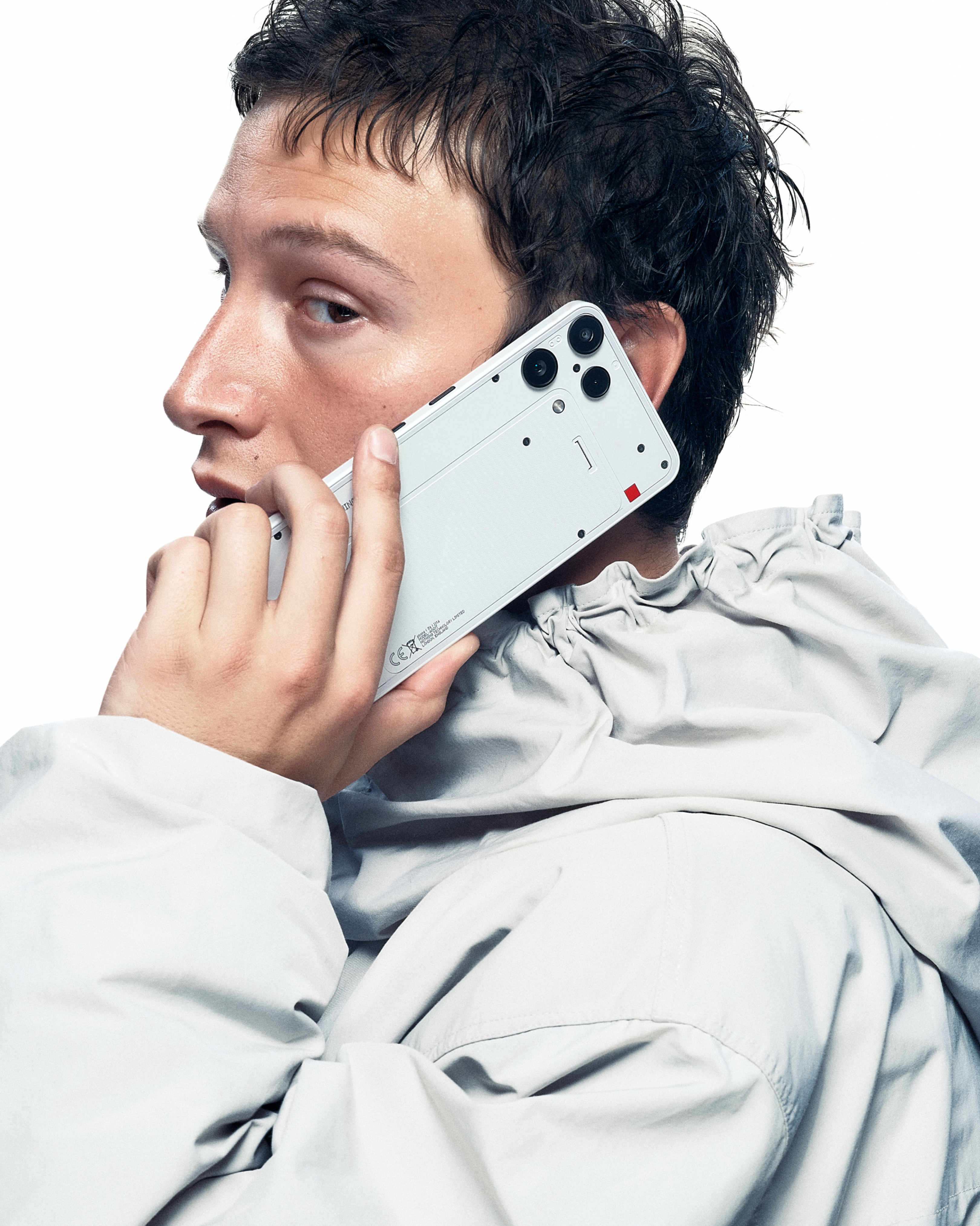 Homme tenant un téléphone blanc à son oreille, portant une veste gris clair.