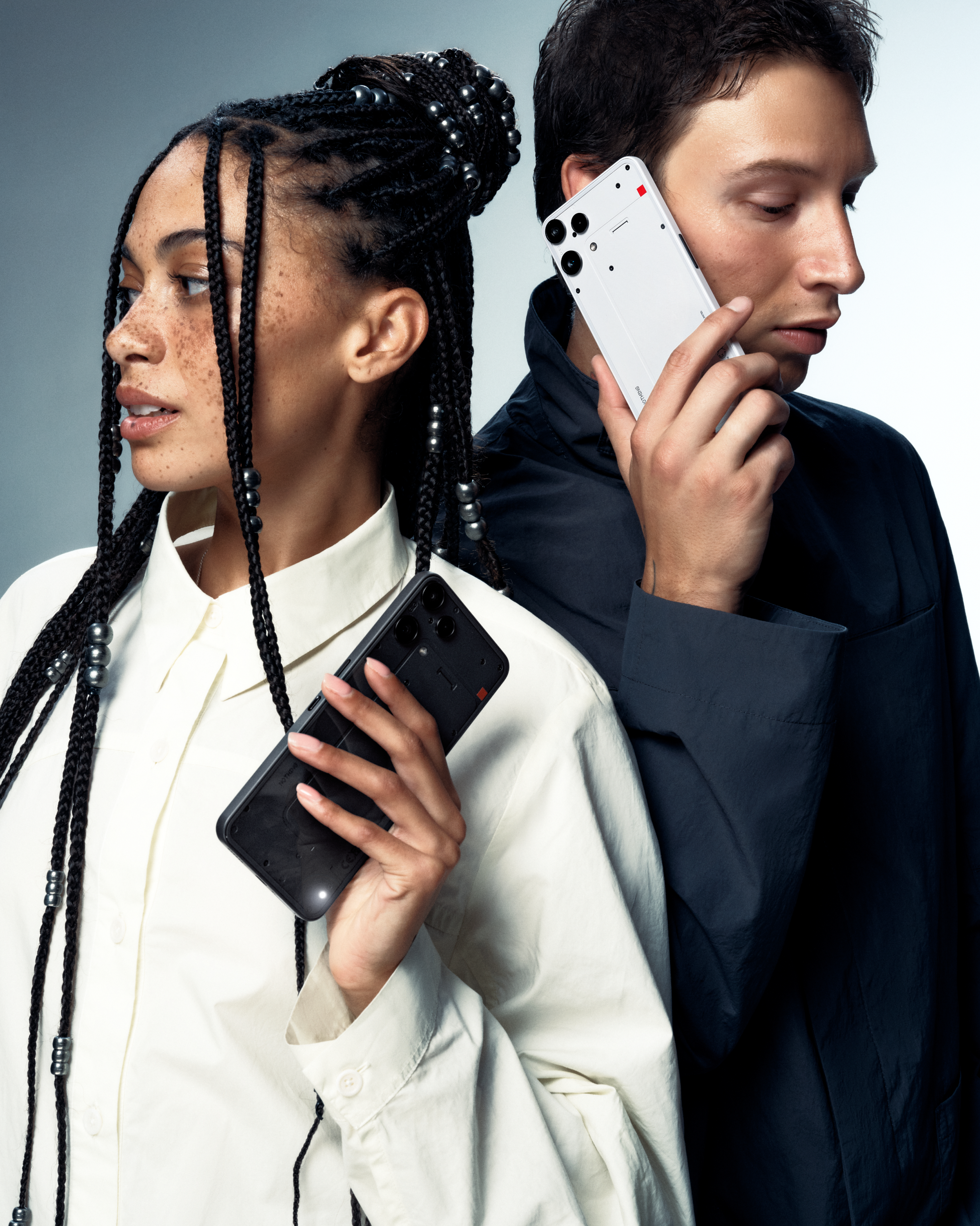 Homme et femme tiennent des téléphones blancs et noirs sur fond gris.