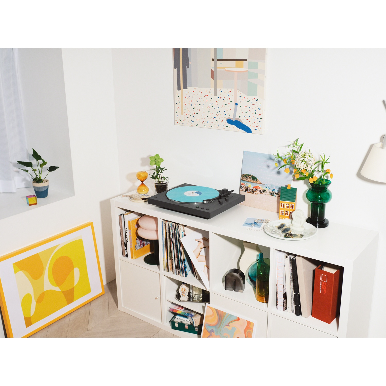 A turntable with a blue record sits on a white shelf surrounded by decor.