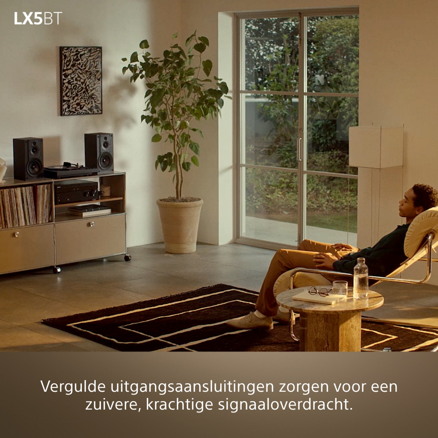Man ontspant zich in een stoel, met stereo-installatie en planten in de kamer.