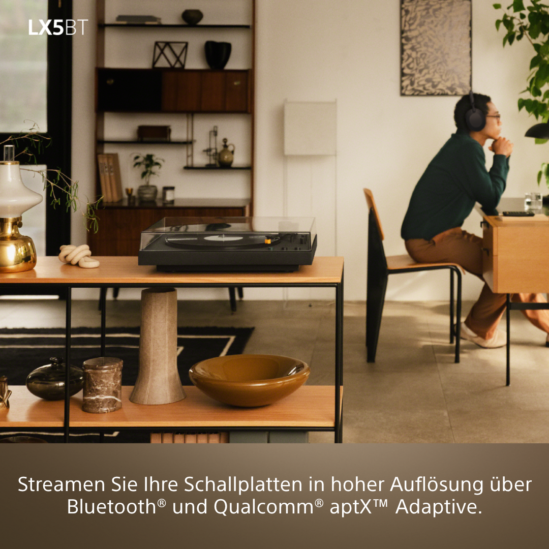 Ein Plattenspieler steht auf einem Regal. Ein Mann hört Musik mit Kopfhörern.