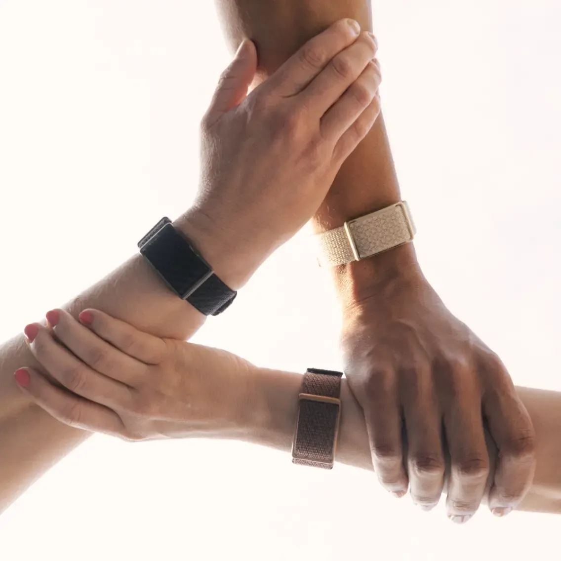 Tres brazos con pulseras se unen en forma de triángulo. Luz brillante.