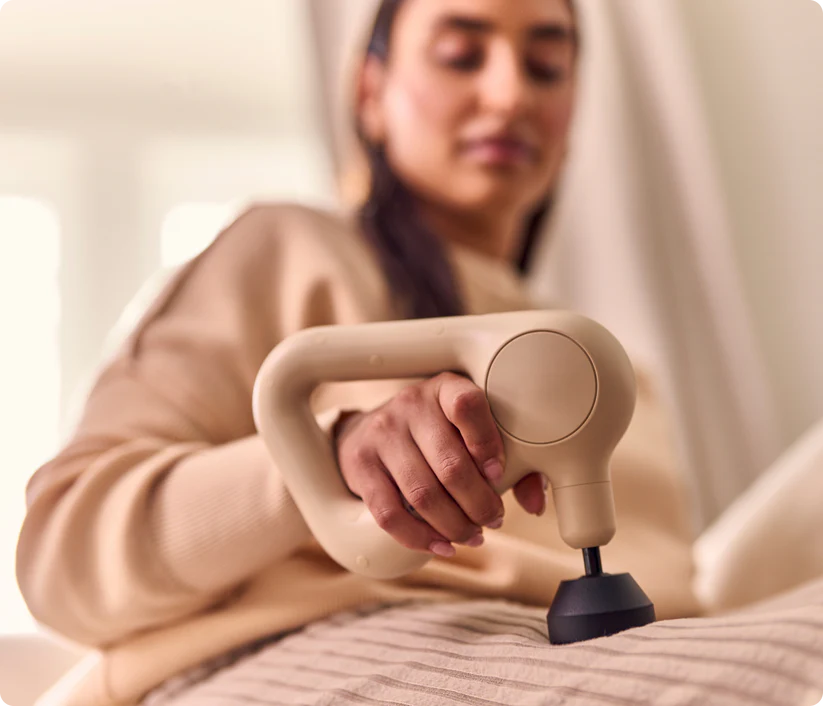 Una mujer usa una pistola de masaje beige en su pierna.