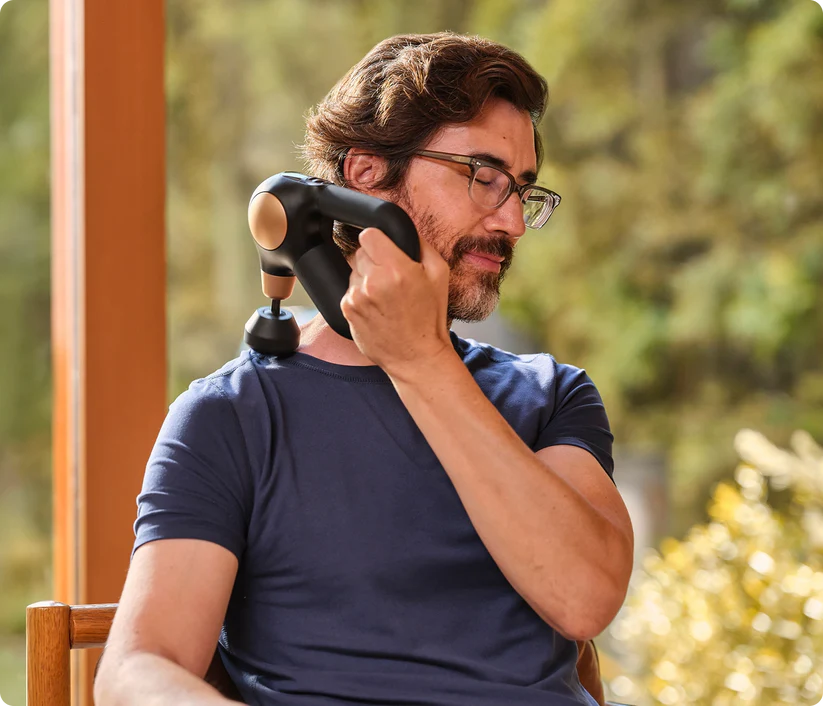 Hombre con gafas usa pistola de masaje en el cuello al aire libre.