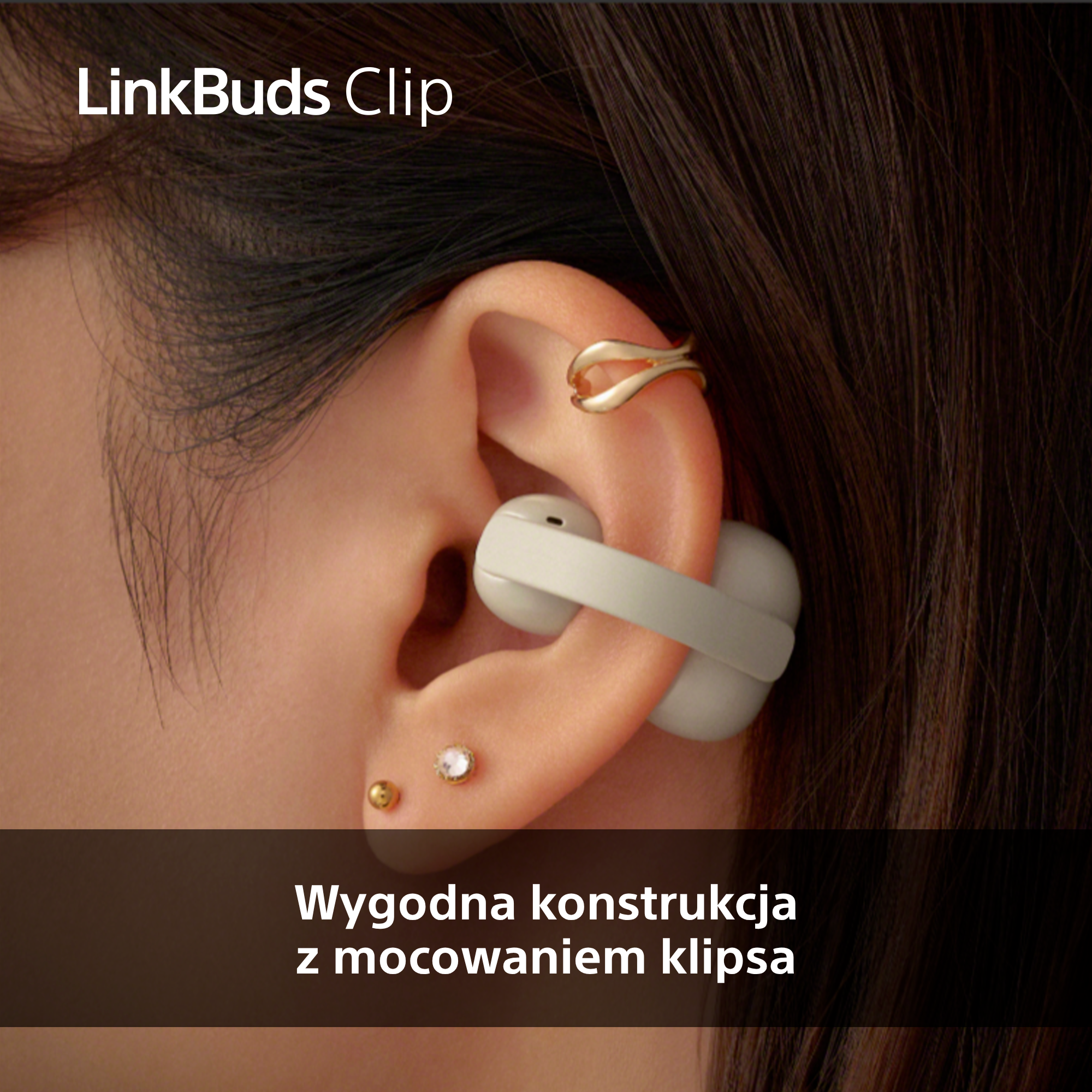Białe słuchawki na klips w uchu, złoty kolczyk, ciemne włosy.