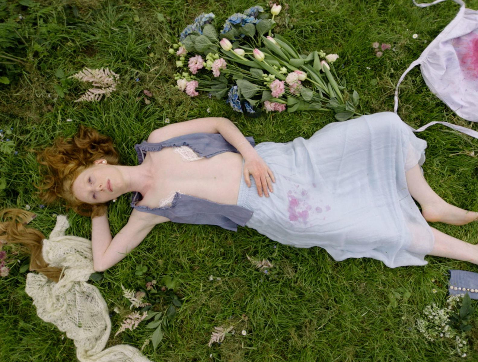 Eine Frau mit roten Haaren liegt auf einer Wiese mit Blumen und Stoff.