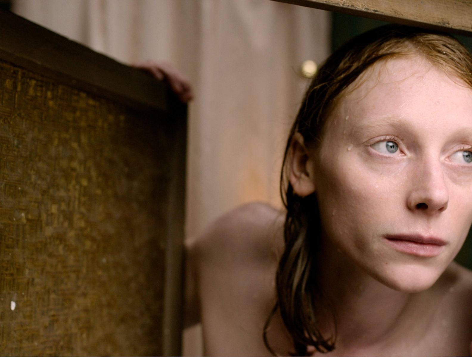 Eine Frau mit roten Haaren und blauen Augen blickt nach rechts. Wassertropfen auf der Haut.