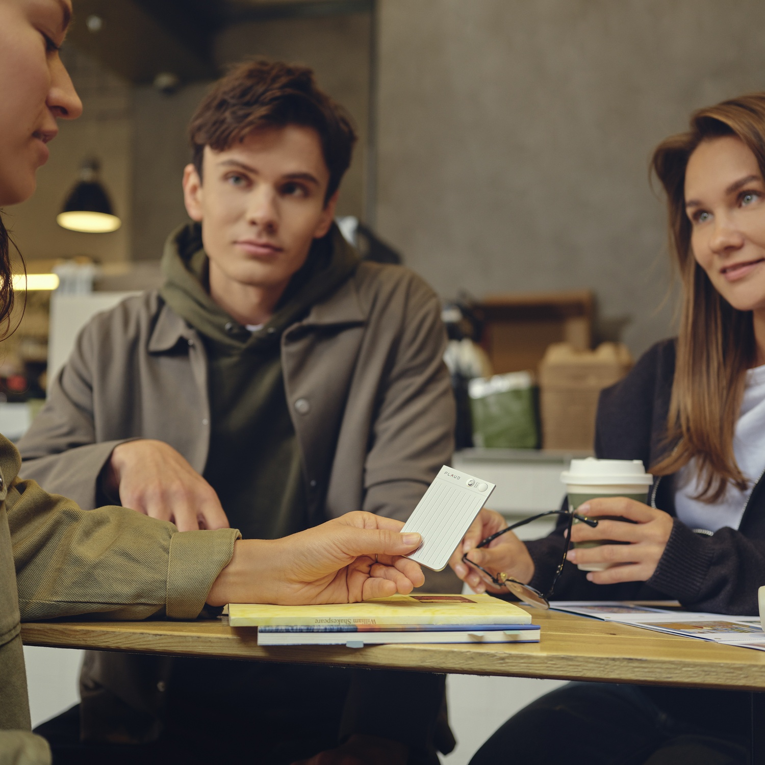 Tre persone sedute a un tavolo, che interagiscono con una carta e una tazza di caffè.