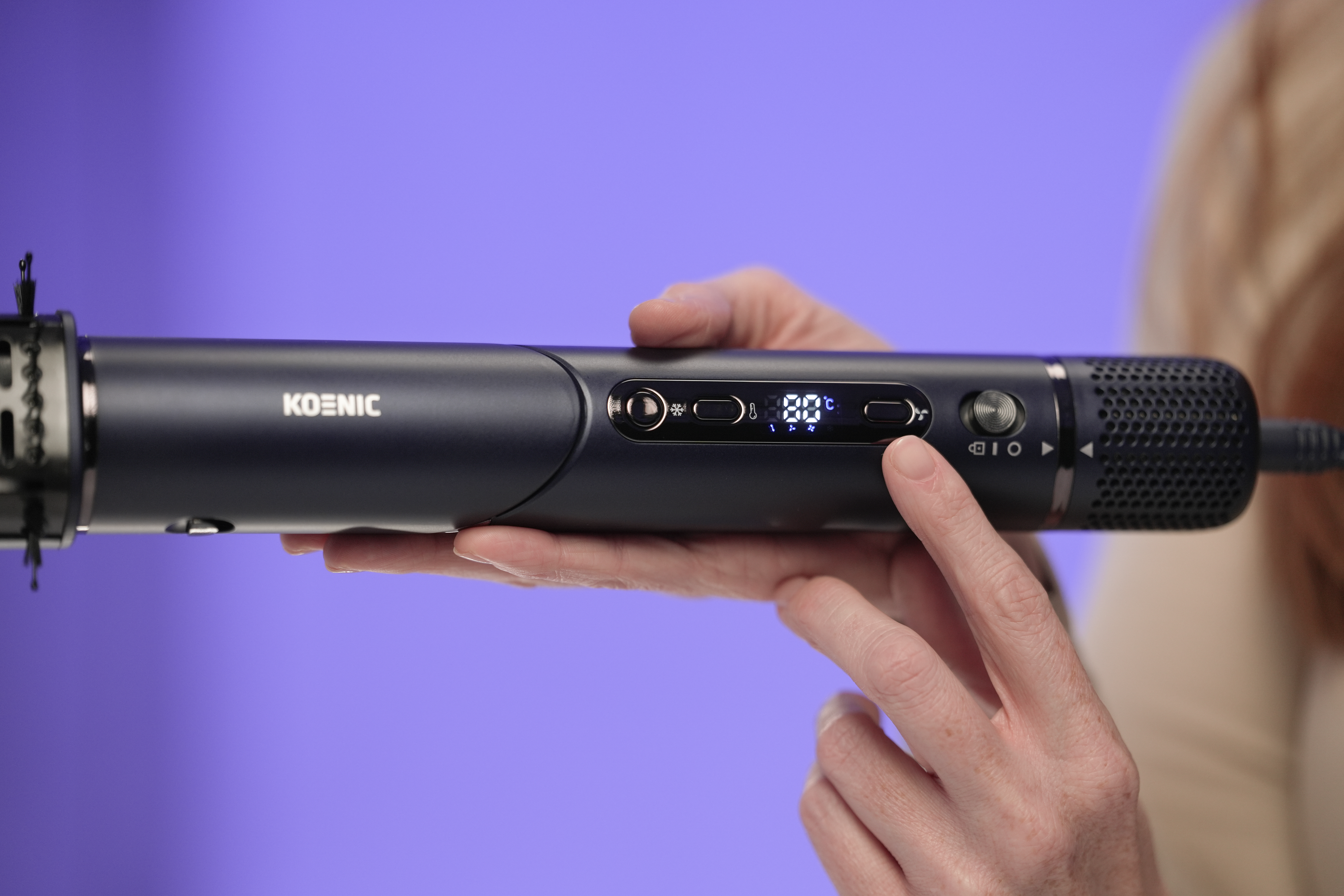 Ciemnoniebieskie urządzenie do stylizacji włosów z cyfrowym wyświetlaczem, trzymane przez rękę.