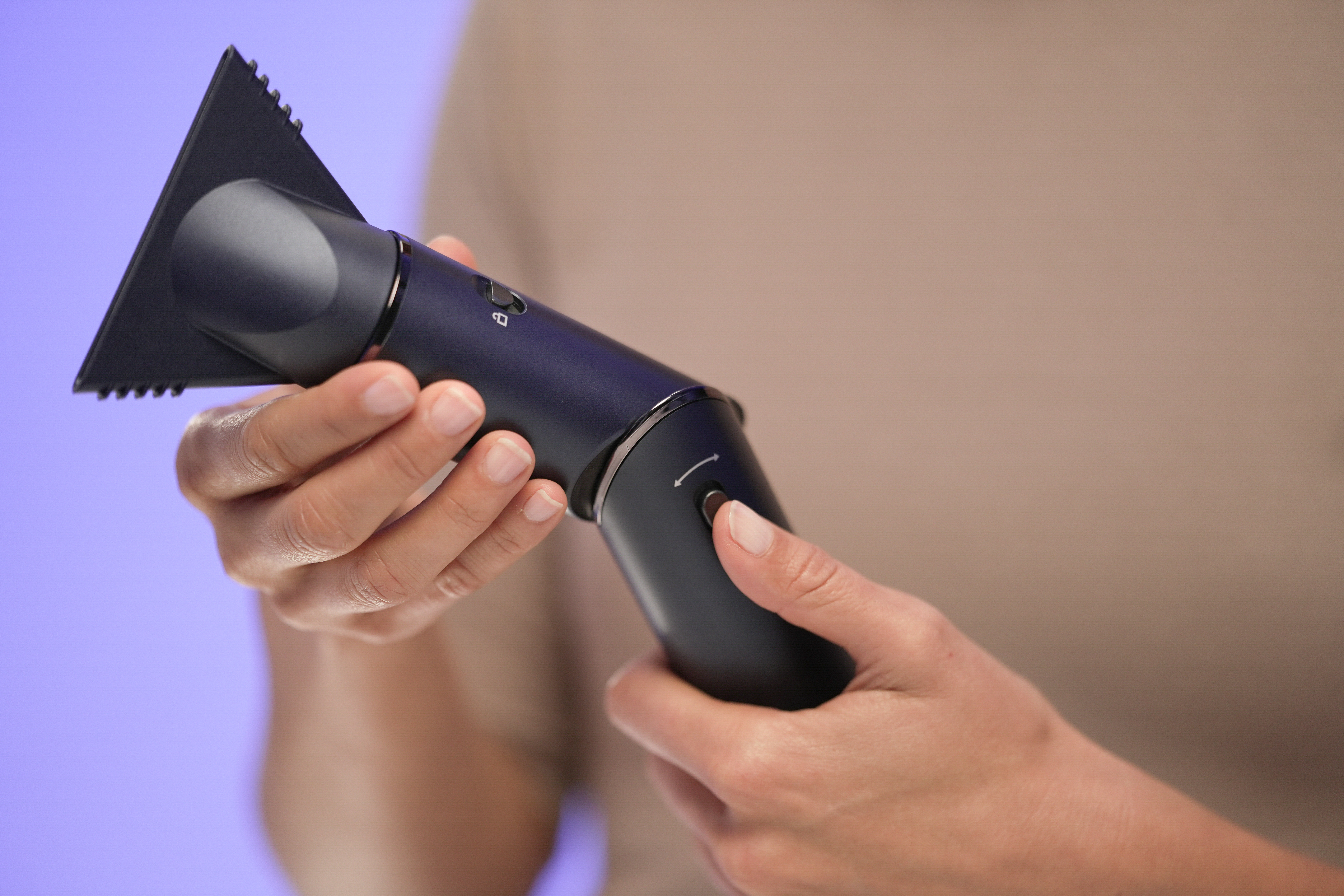 Ciemnoniebieskie urządzenie domowe z trójkątną dyszą, trzymane przez dłonie.