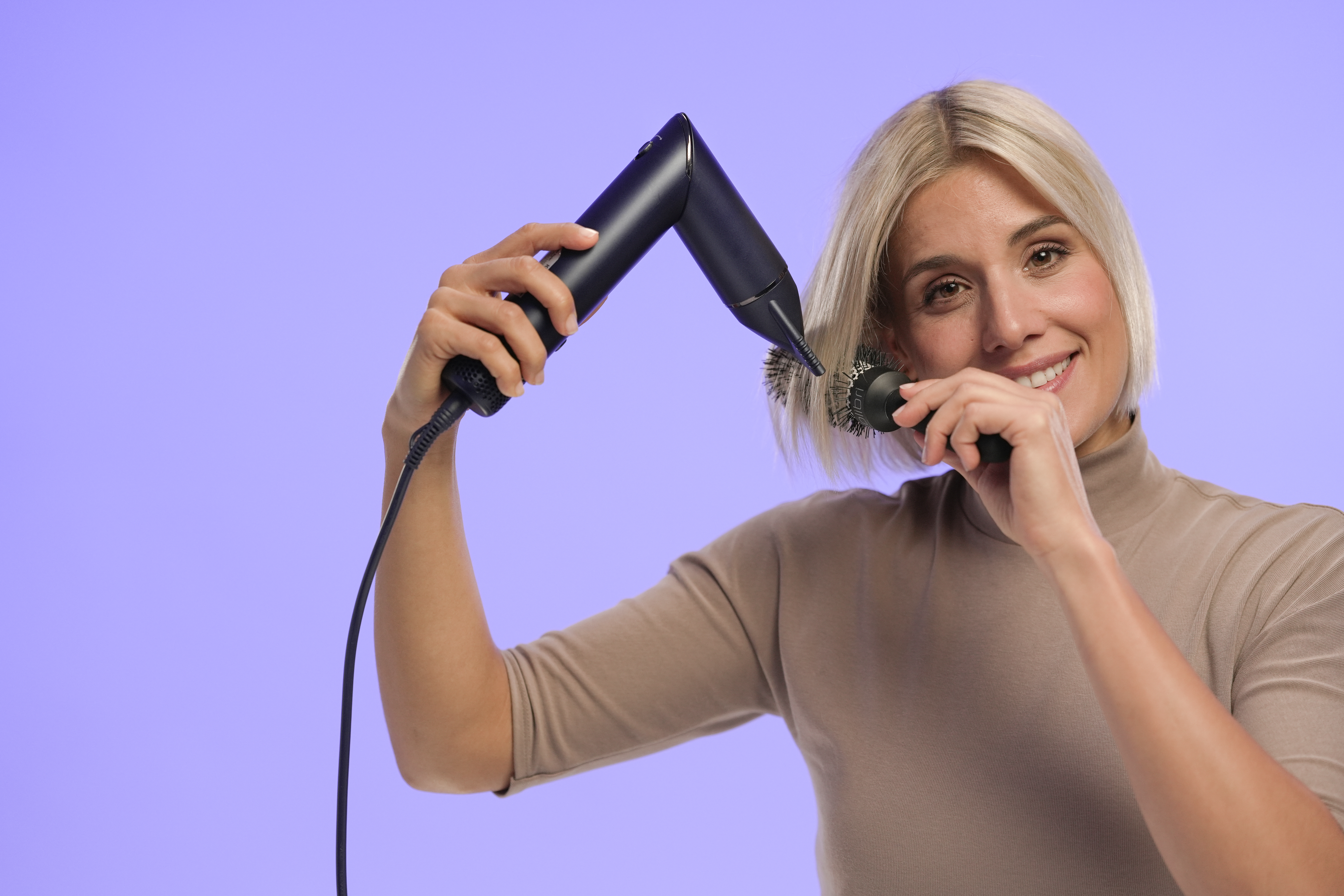 Kobieta z blond boba suszy włosy czarną suszarką i okrągłą szczotką.