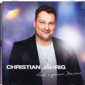 Mann mit dunklem Jackett und Kette lächelt, vor verschwommenem Hintergrund.
