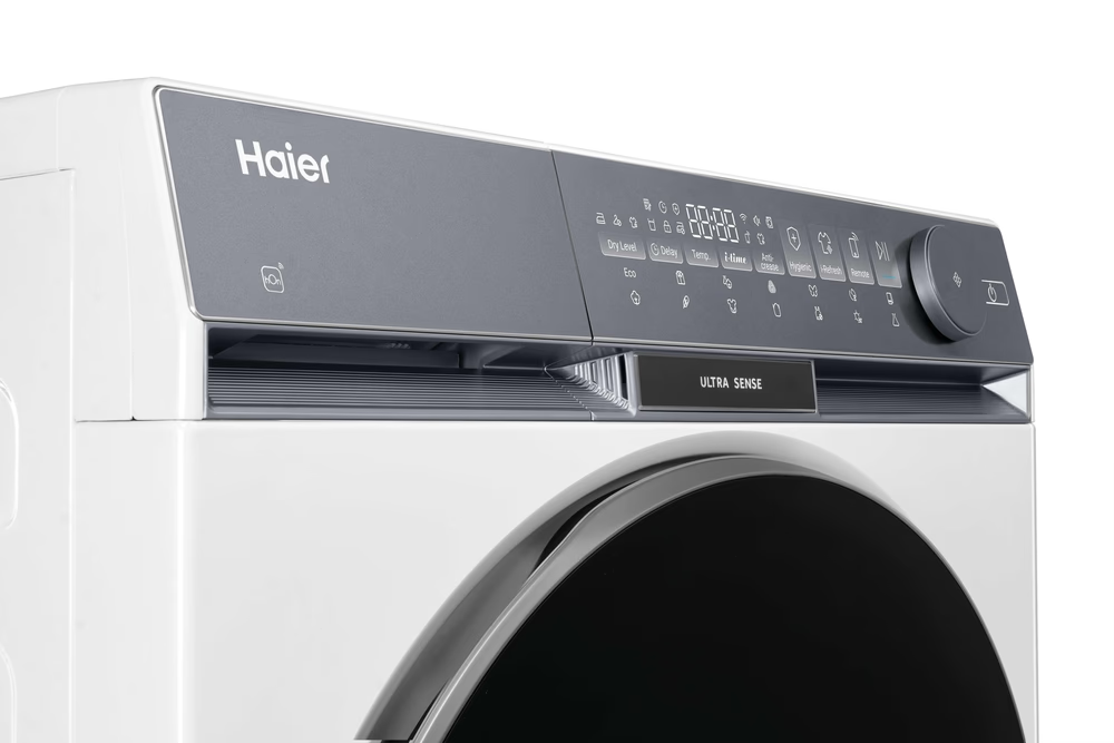 Fehér Haier mosógép digitális kezelőpanellel és kerek tárcsával, közelről.