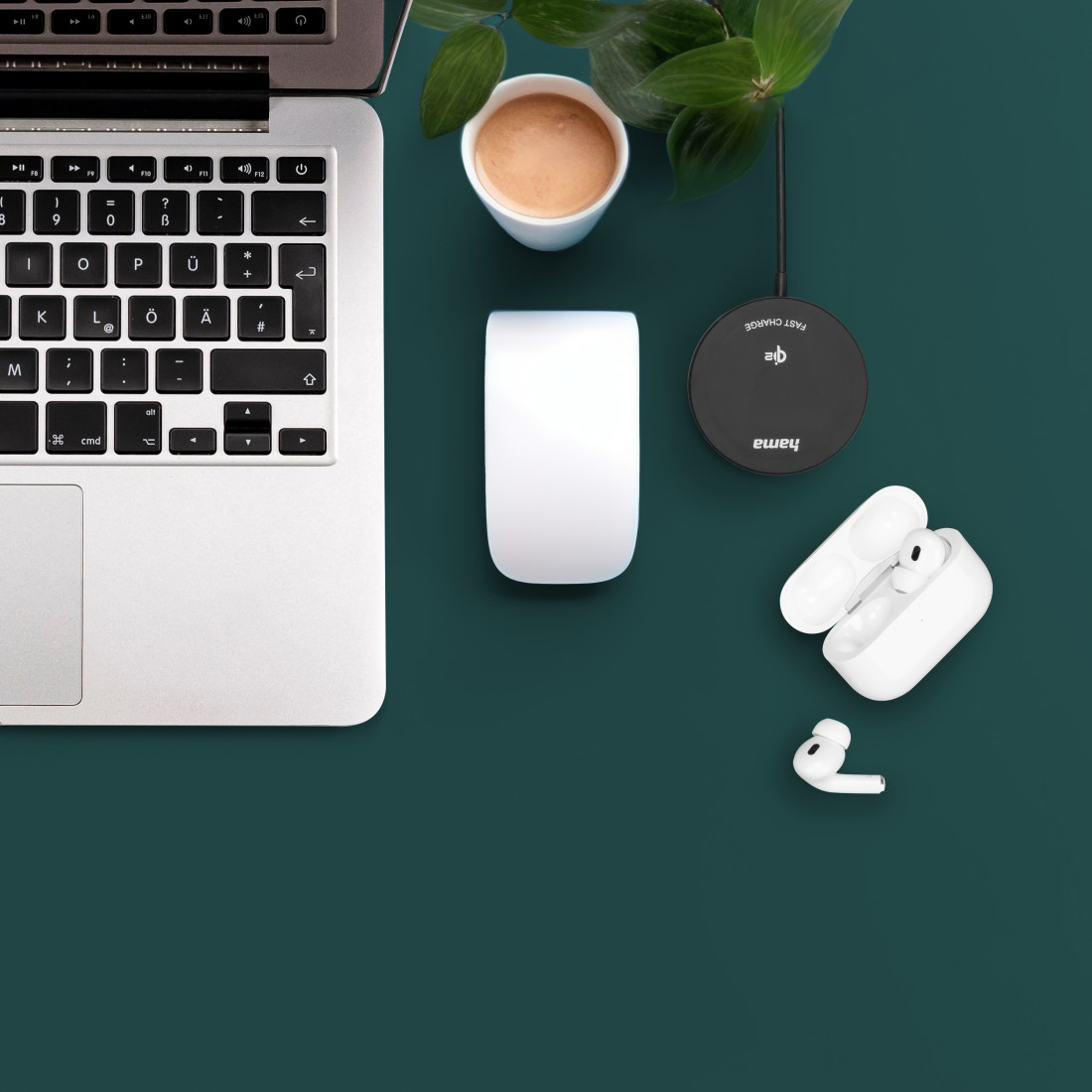 Laptop, fehér egér, AirPods, kávéscsésze és töltő sötét háttéren.