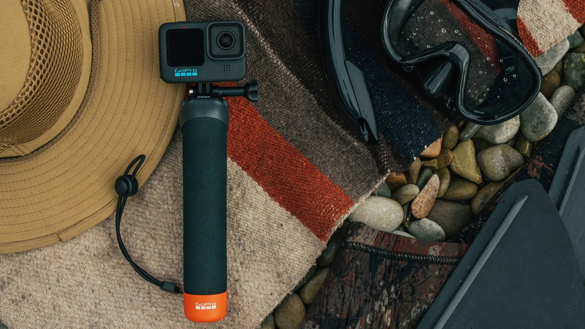 GoPro, Hut, Schnorchelausrüstung und Decke auf Kieselsteinen.