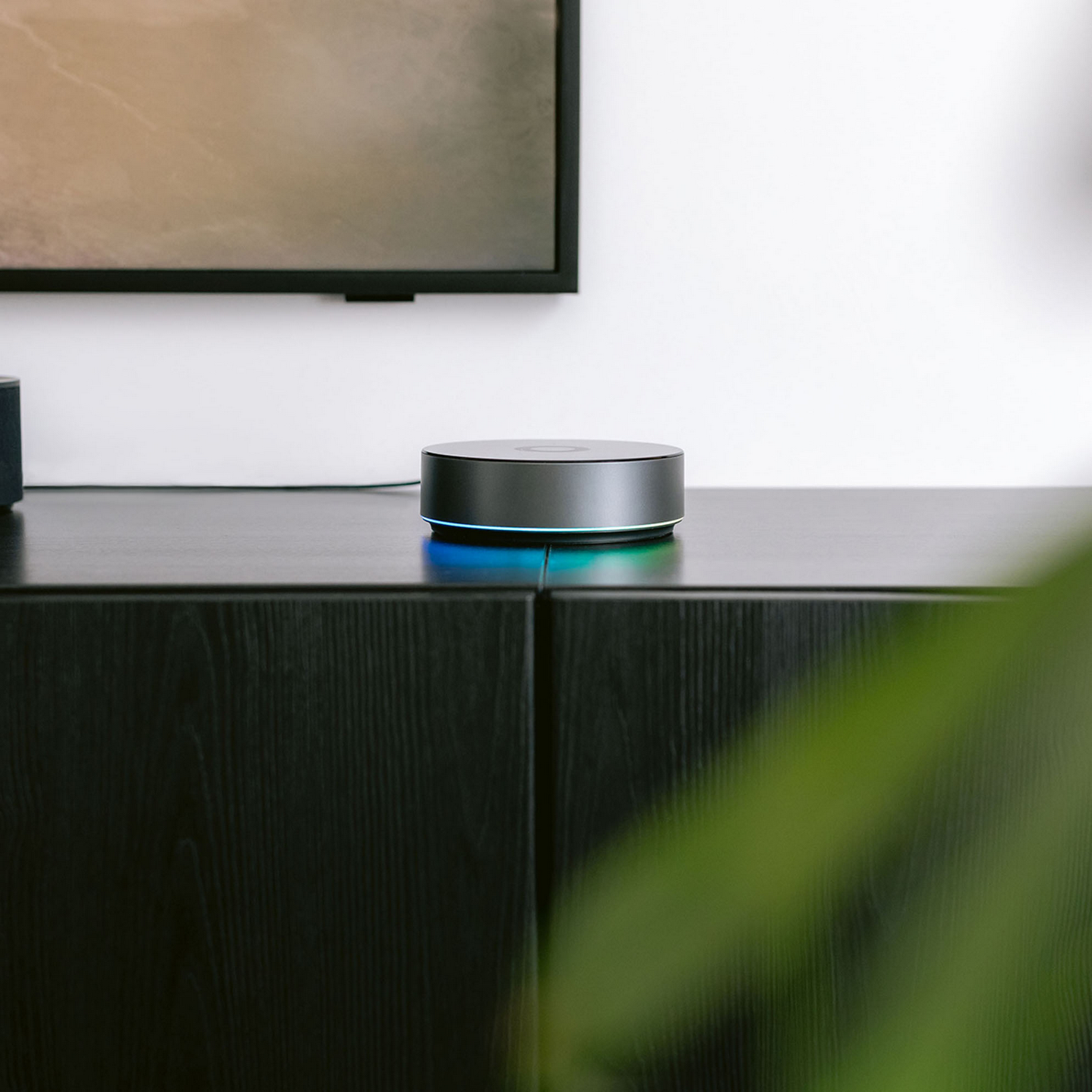 Un altavoz inteligente gris con luz azul sobre un mueble negro.