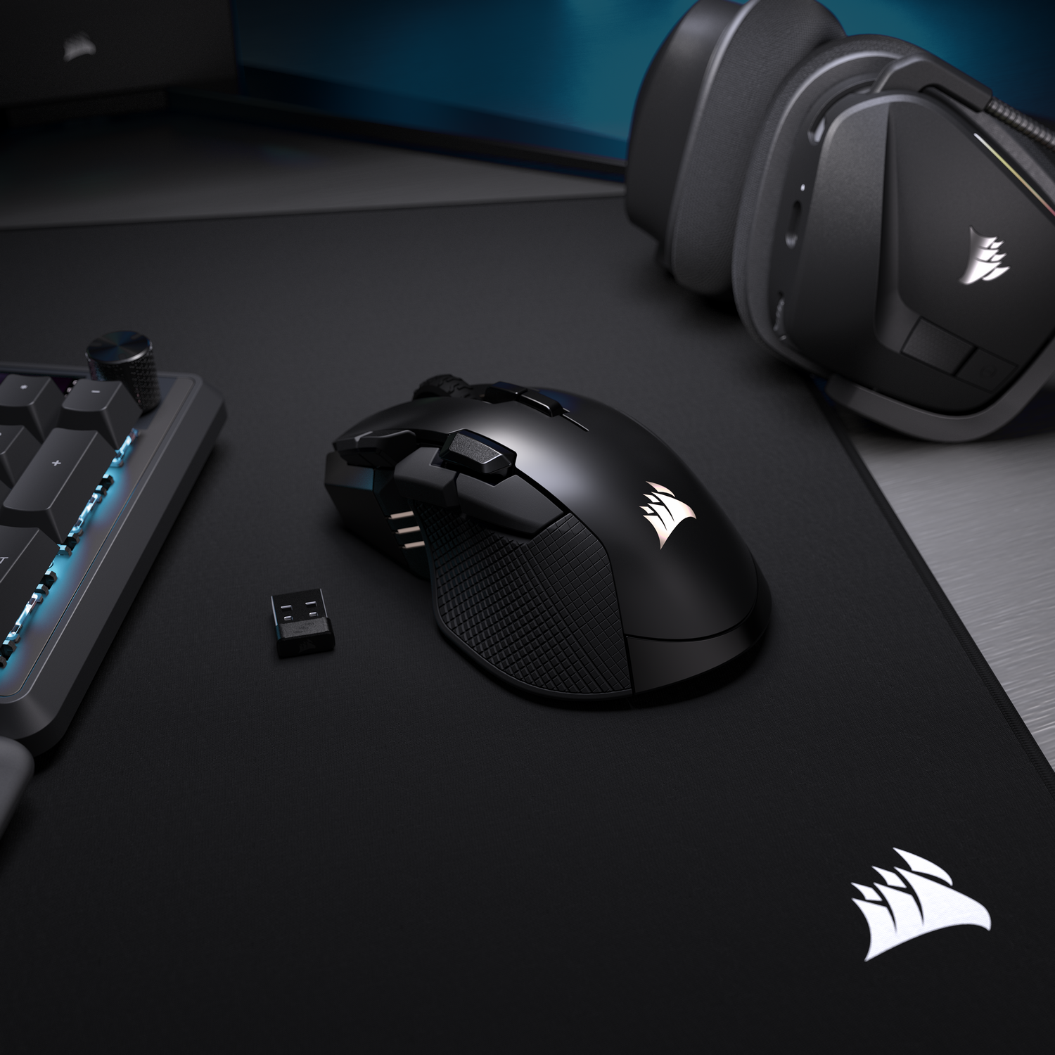Ratón, teclado y auriculares negros para juegos sobre una alfombrilla negra.
