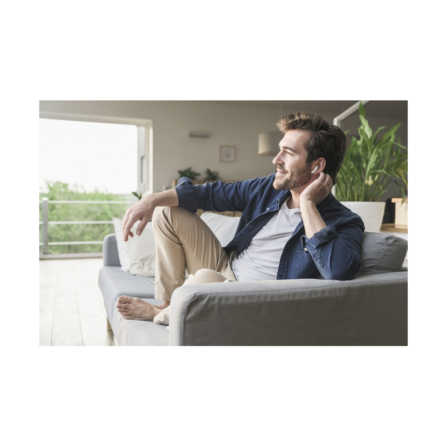 Un uomo siede su un divano, ascoltando musica con auricolari wireless.