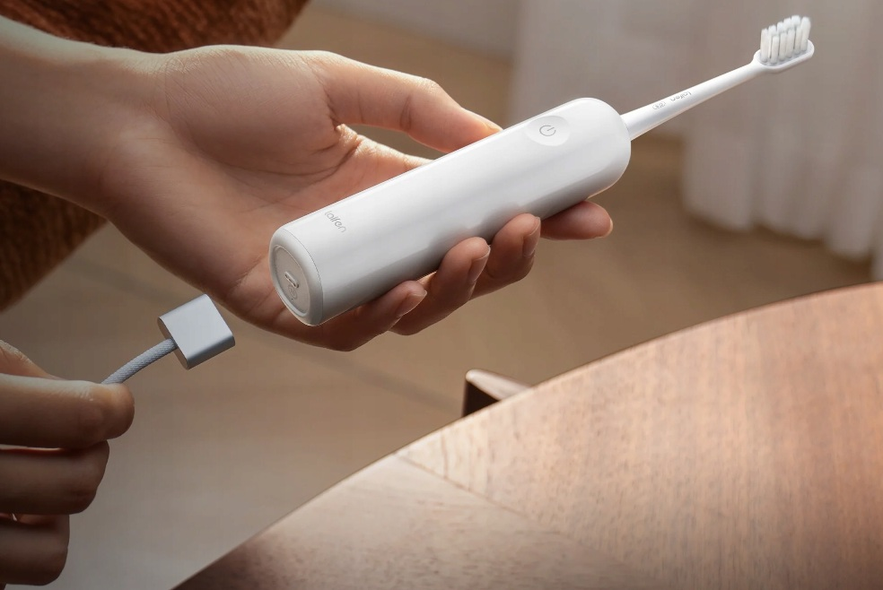 Dłoń trzyma białą szczoteczkę elektryczną z kablem ładującym.