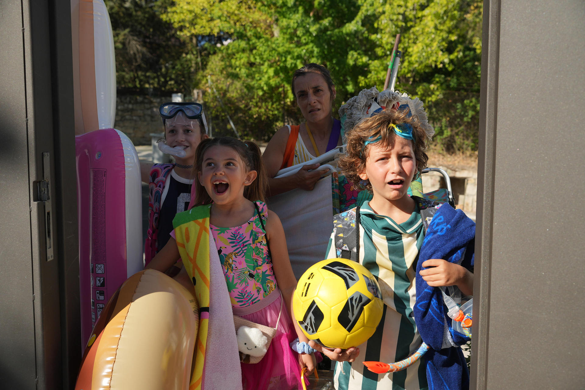 Kinder mit Schwimmbrillen und aufblasbaren Spielzeugen blicken erwartungsvoll.